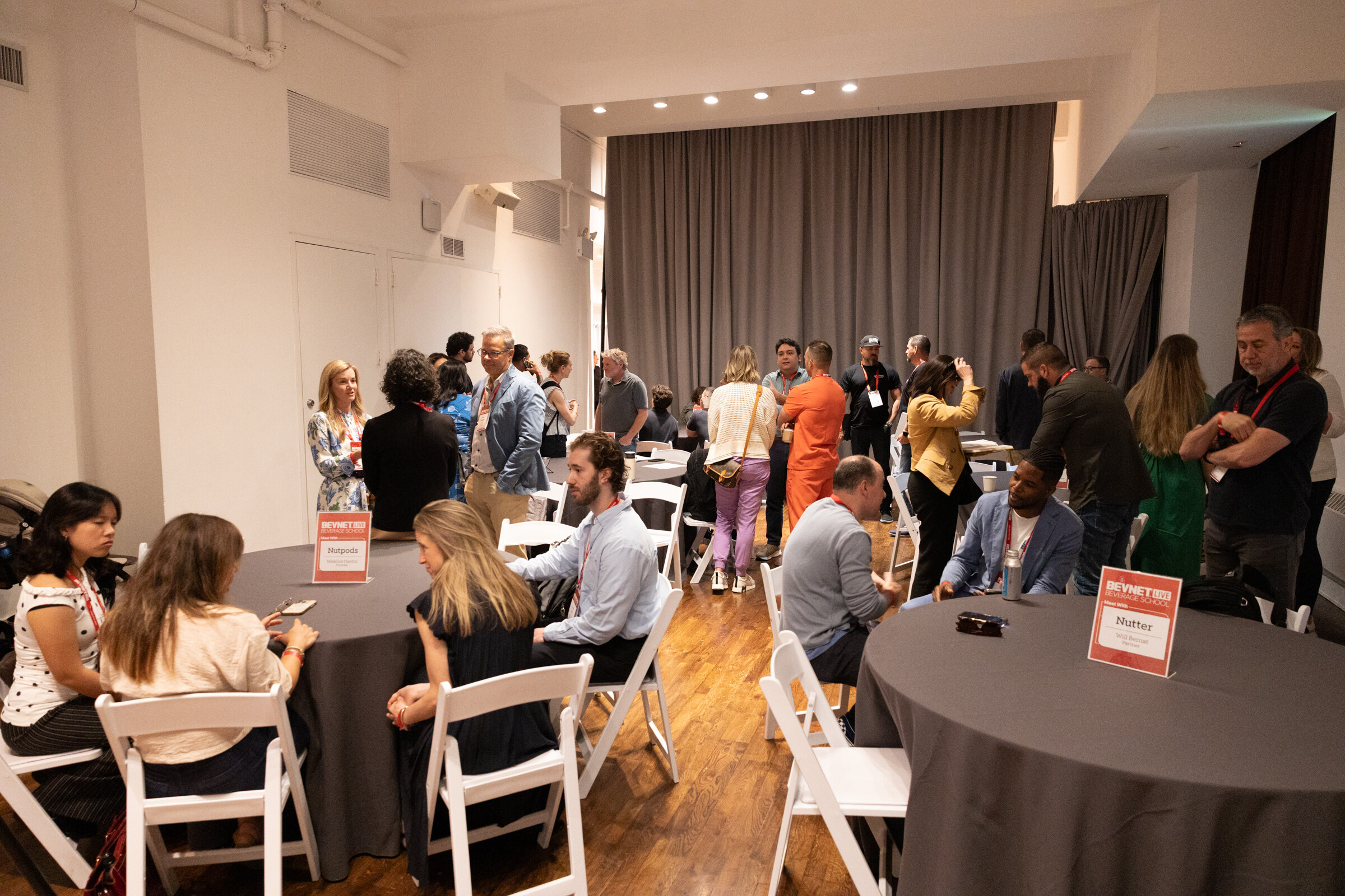 Room of round tables with “Meet With” cards for Nutpods and Nutter, attendees seated and standing in groups.