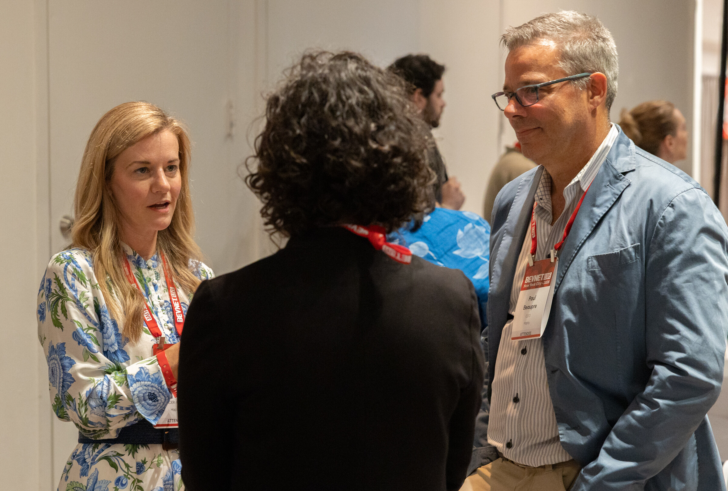 Woman in a floral blouse talking with two attendees, one in a blue blazer.