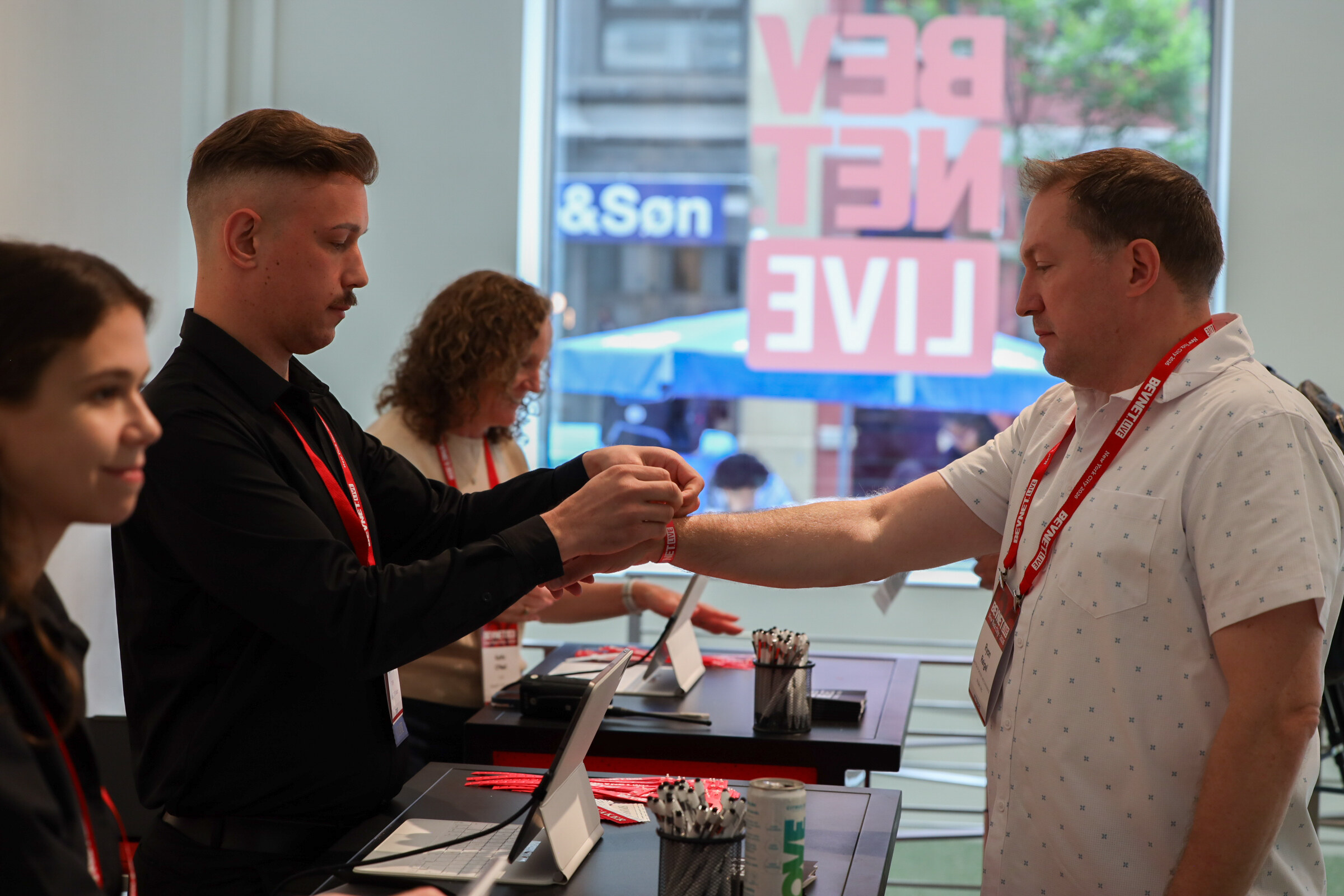 Staff member fastening a wristband on an attendee at the check-in counter, with a large BevNET Live decal on the window behind them.