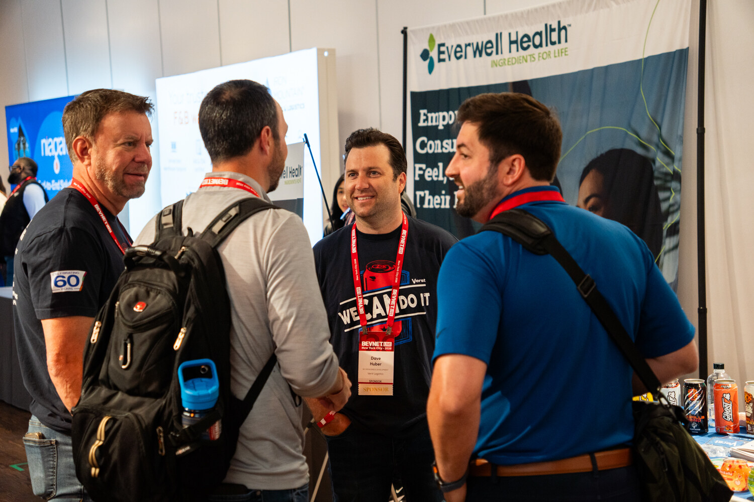 Four men talking and smiling in front of an Everwell Health banner on the expo floor.