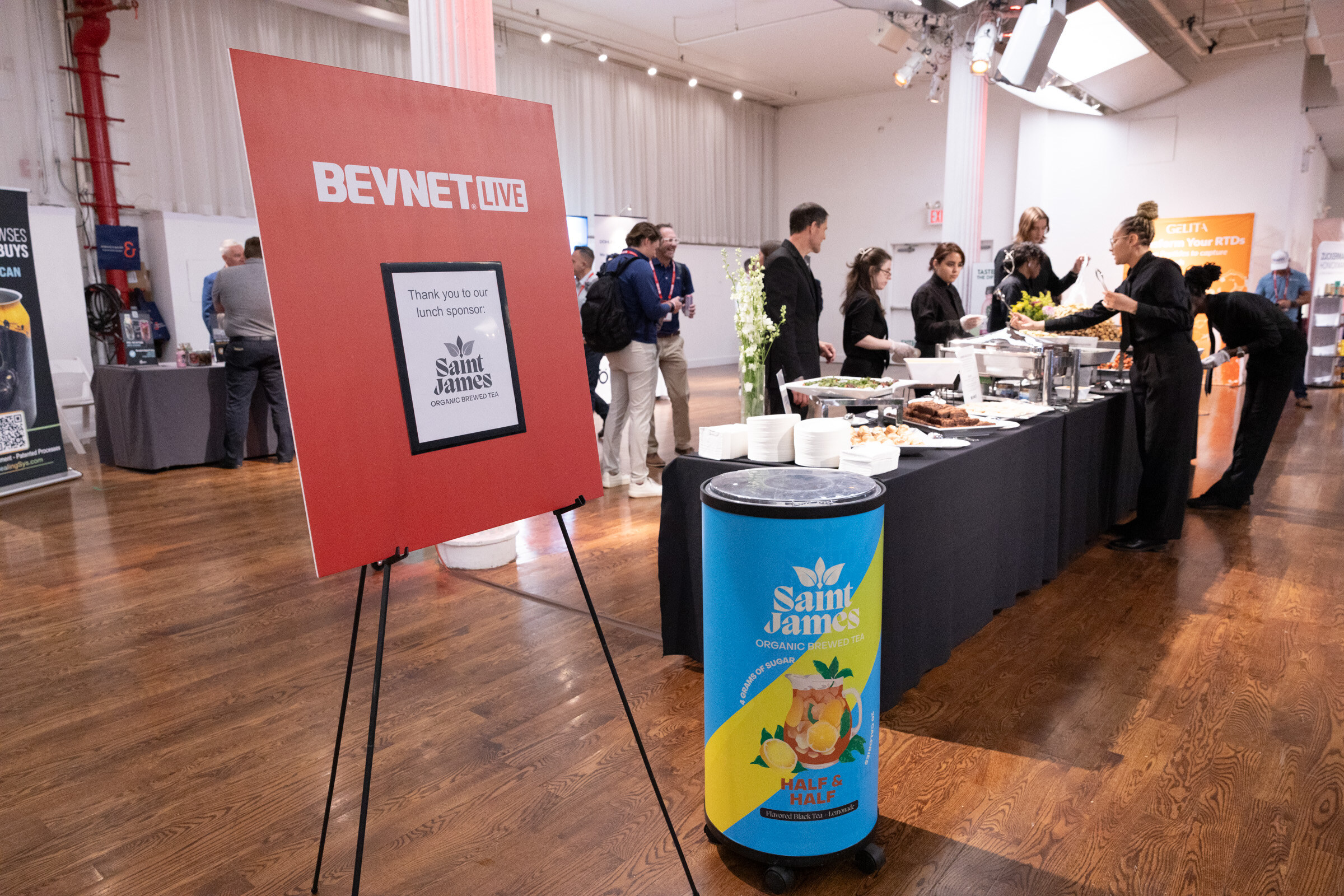Red BevNET Live easel sign thanking lunch sponsor Saint James, beside a Saint James cooler and a long buffet line.
