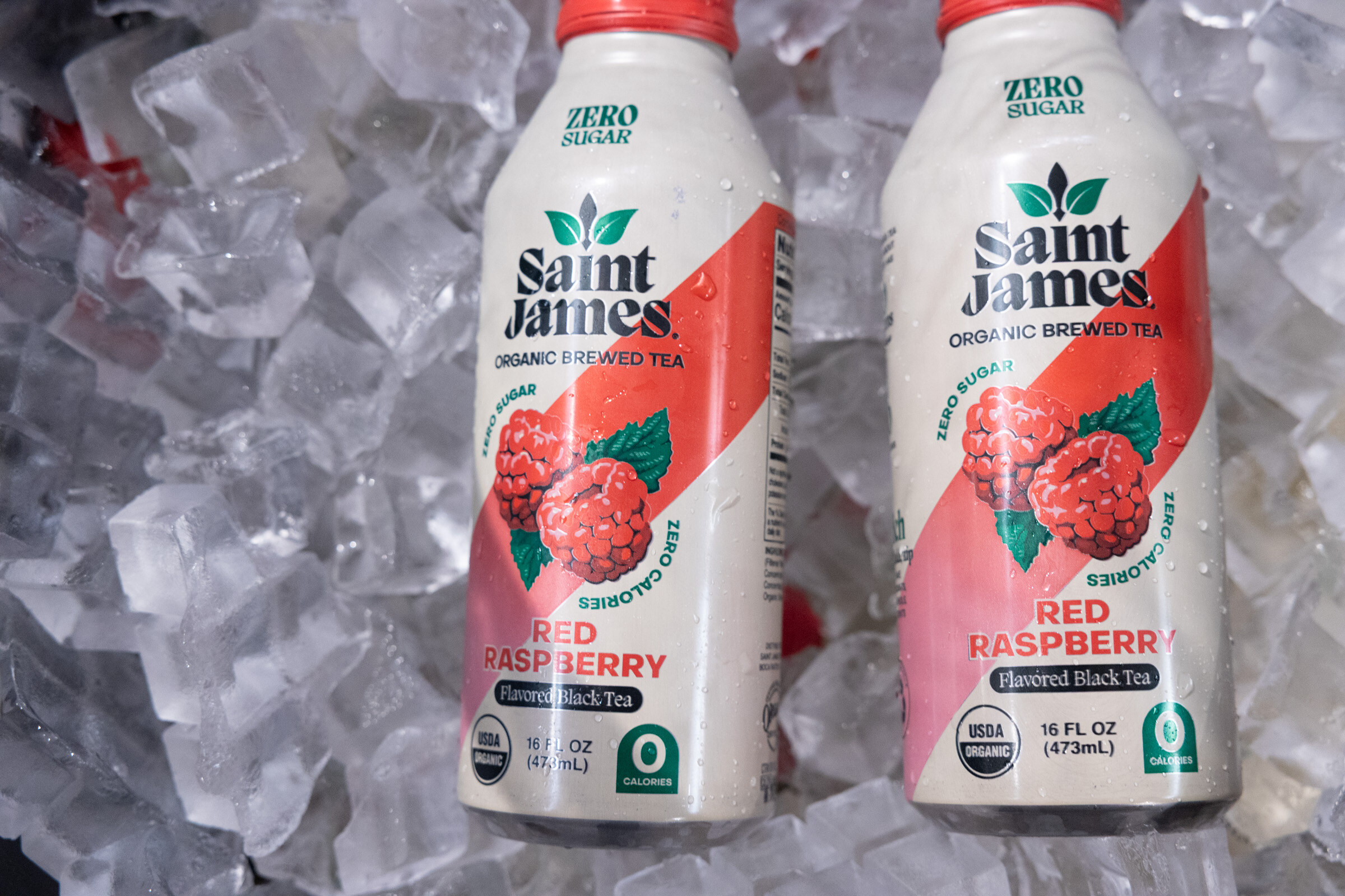 Two bottles of Saint James zero sugar Red Raspberry organic brewed tea nestled in ice.