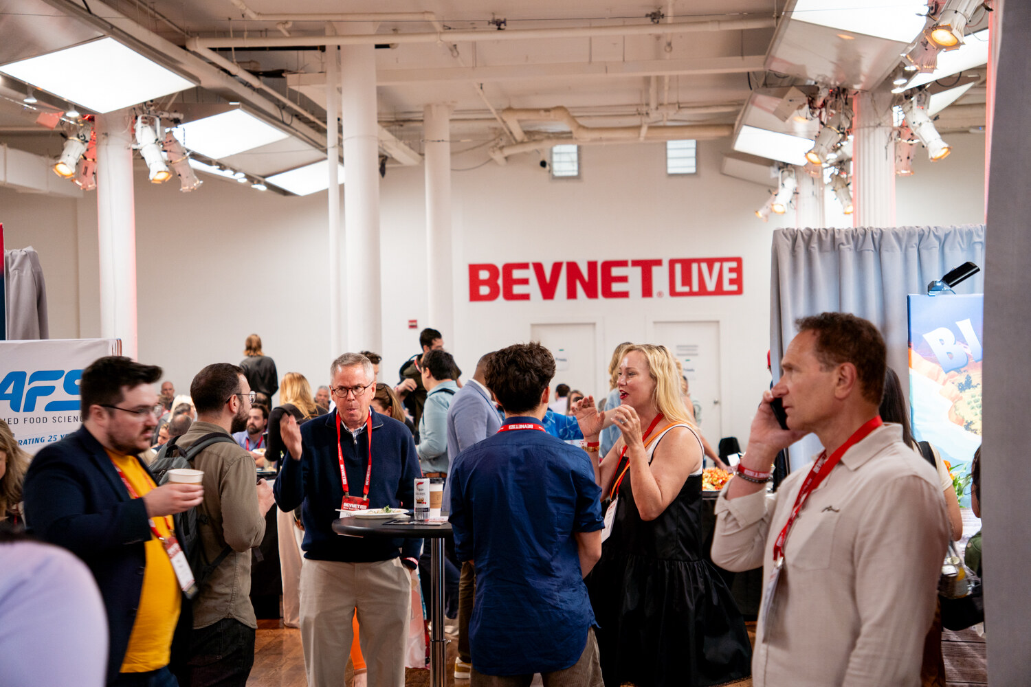 Attendees standing and talking around high-top tables in a white hall with a red BevNET Live sign on the back wall.