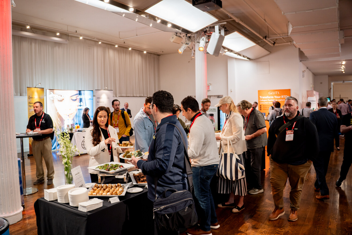 Attendees with plates lining up along a buffet table on the main floor, with sponsor booths behind.