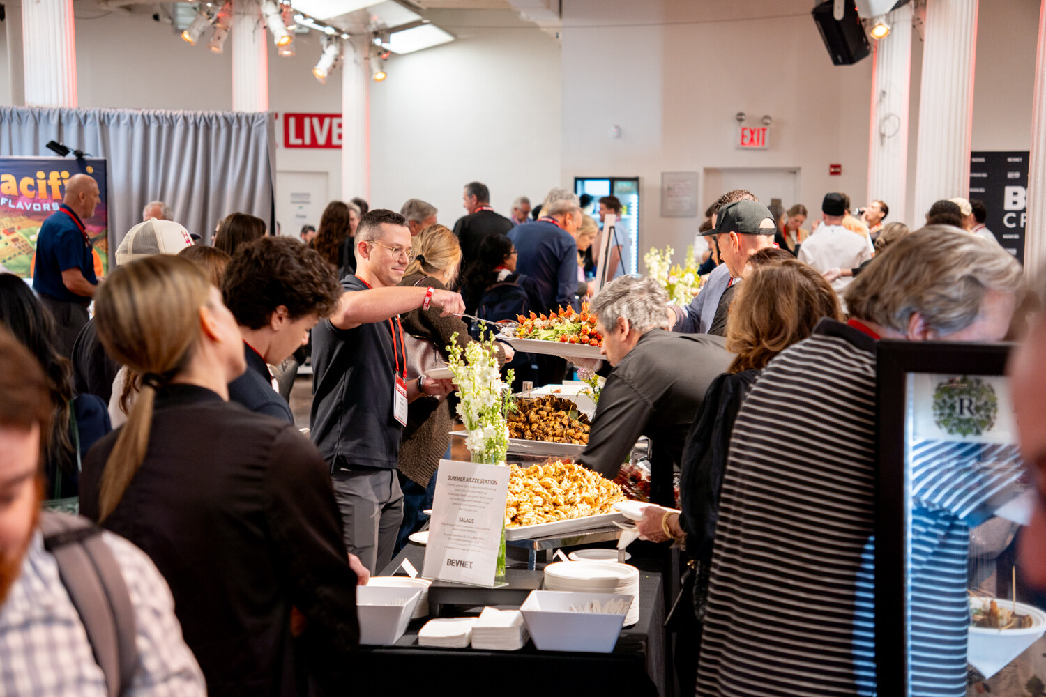 A crowd of attendees serving themselves from a buffet of salads and bites decorated with flowers.