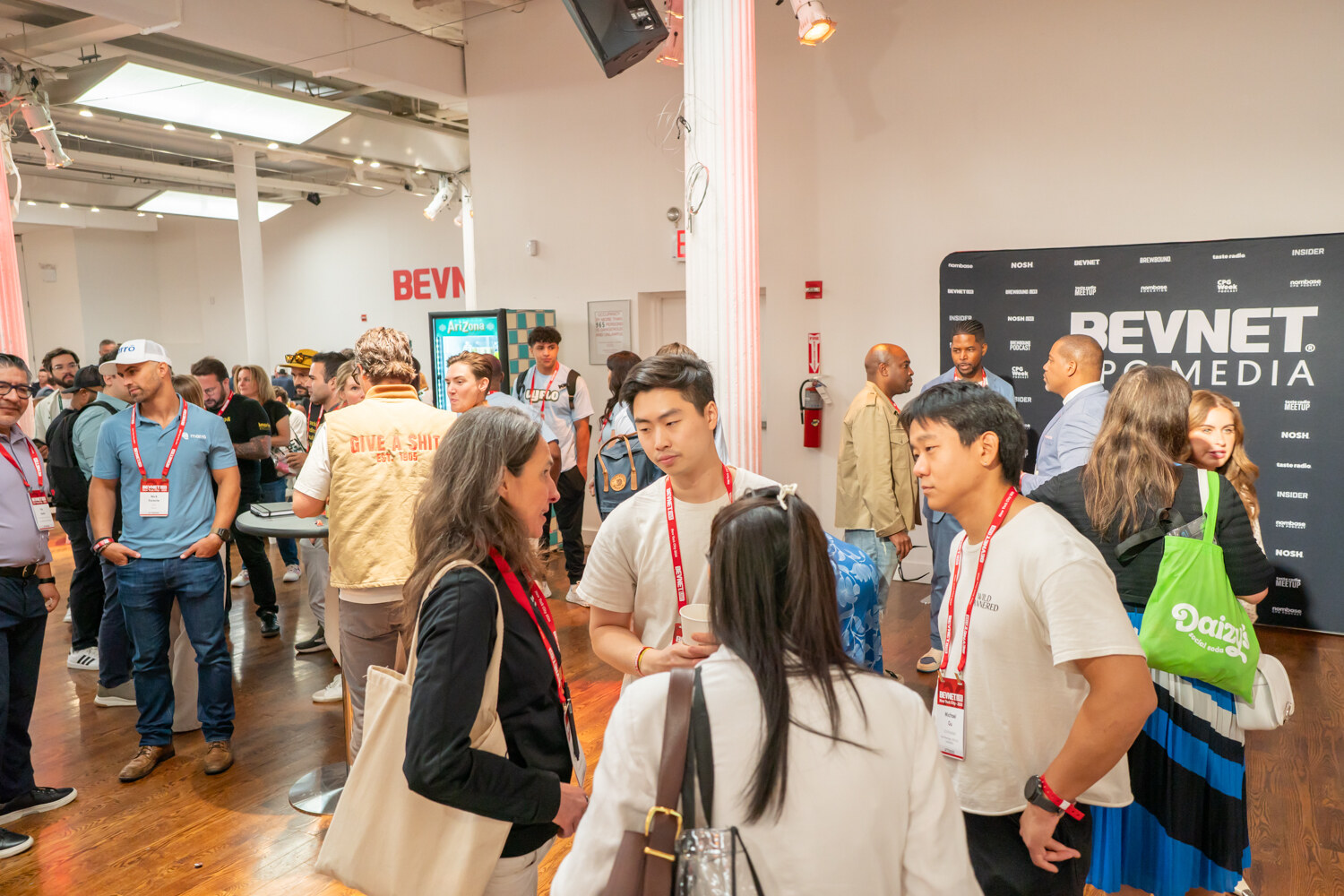Groups of attendees talking on a hardwood floor near a black BevNET CPG Media step-and-repeat backdrop.