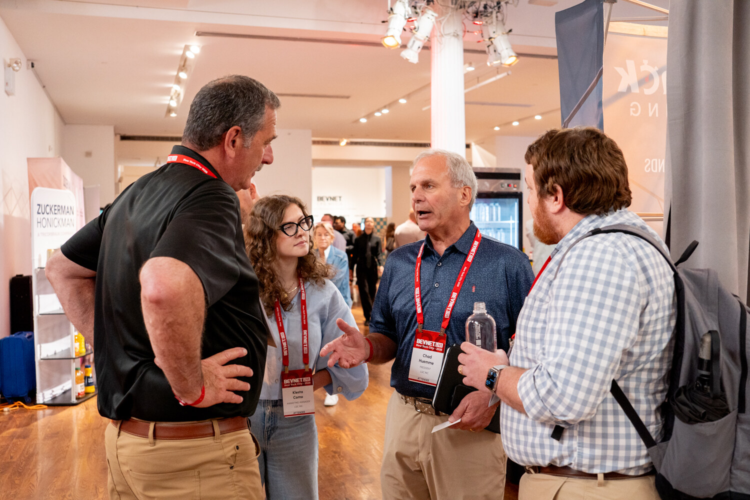 Older man in a navy polo talking with three attendees, one woman and two men, on the expo floor.