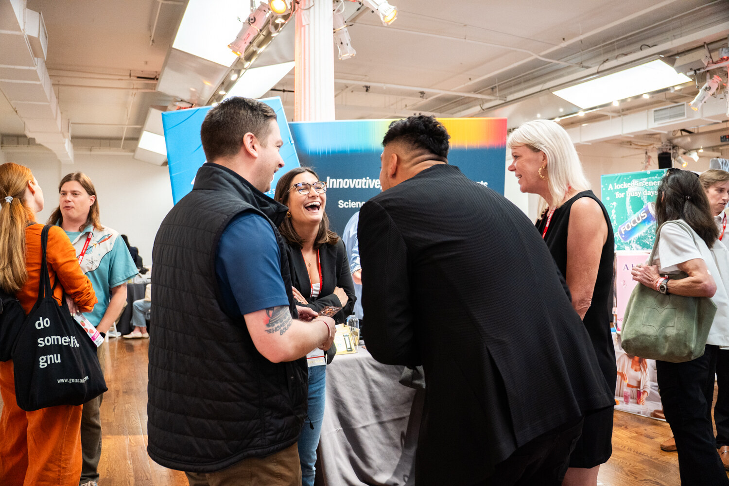 Woman laughing broadly while talking with three other attendees at a sponsor booth.