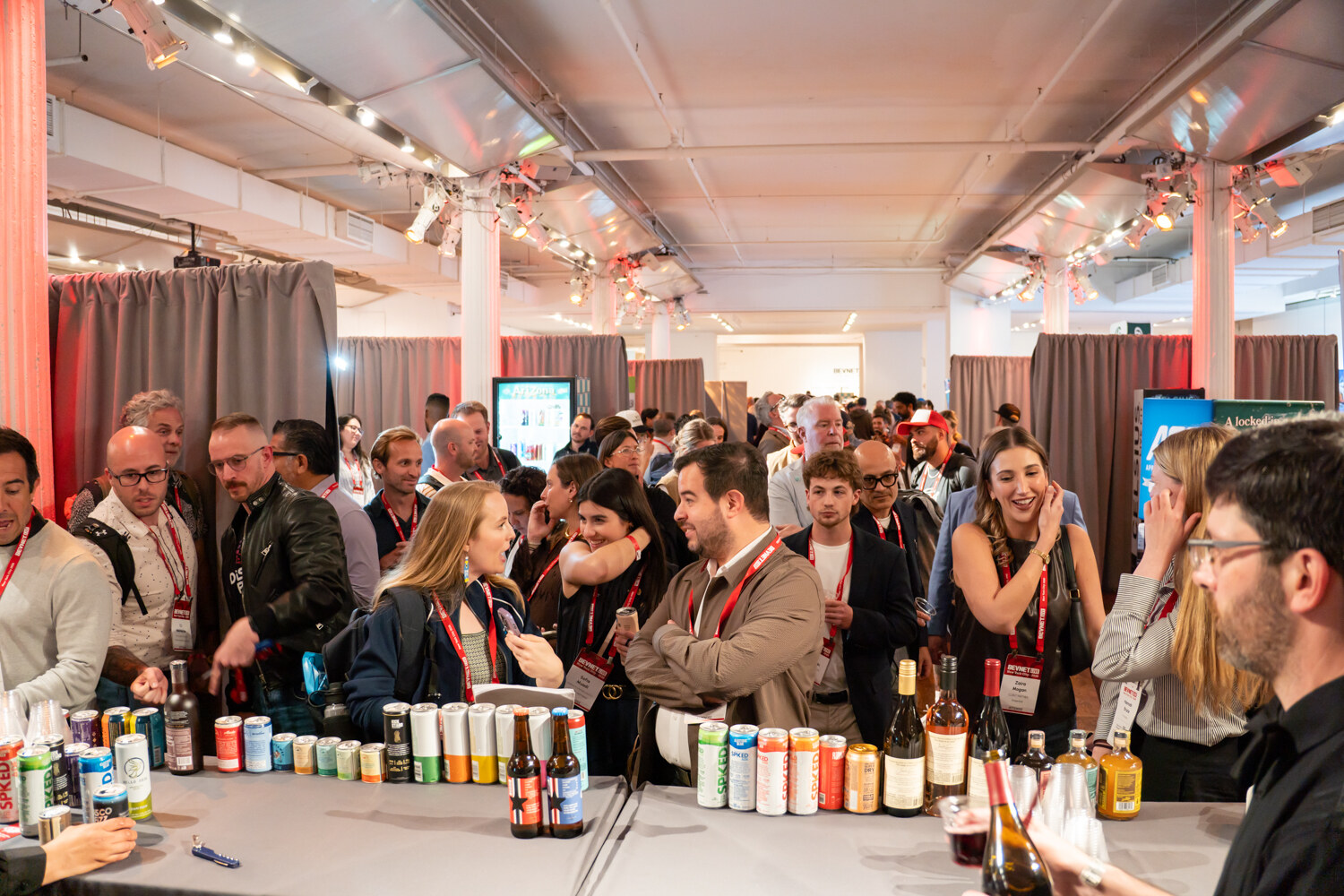 A crowd of smiling attendees behind a long table lined with cans and bottles at the start of the happy hour.