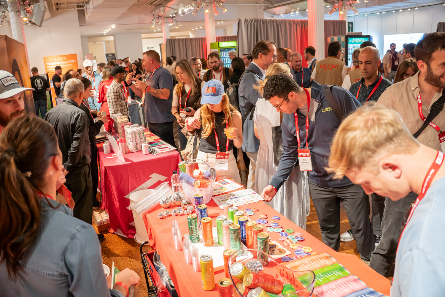 Attendees leaning over a long orange table covered in cans and samples during the happy hour.