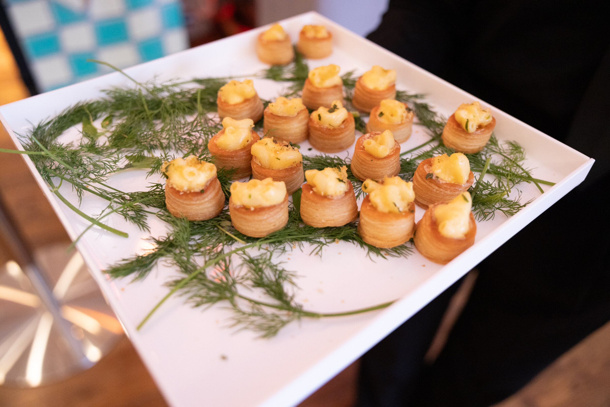 White tray of small puff pastry bites garnished with dill.