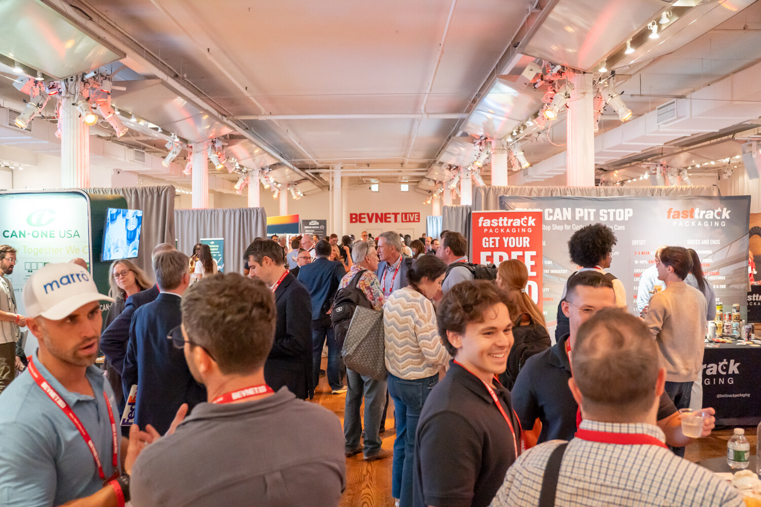 A dense crowd of attendees talking and laughing on the expo floor under a BevNET Live sign.