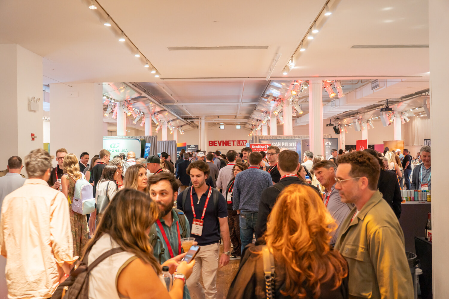 Wide view of a packed hall of attendees with drinks, several turned toward one another in conversation.
