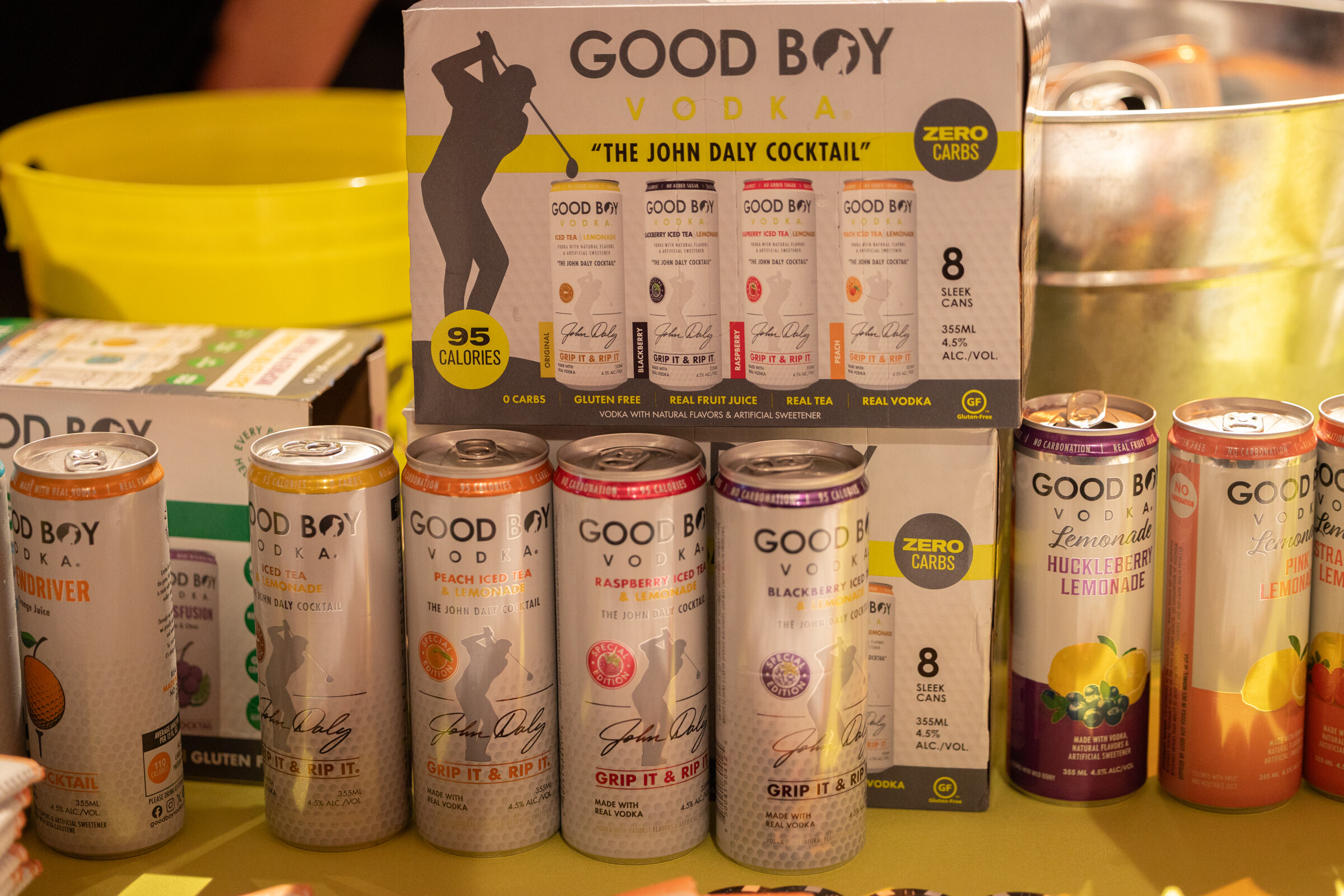 Cans and an eight-pack box of Good Boy Vodka cocktails on a yellow table.