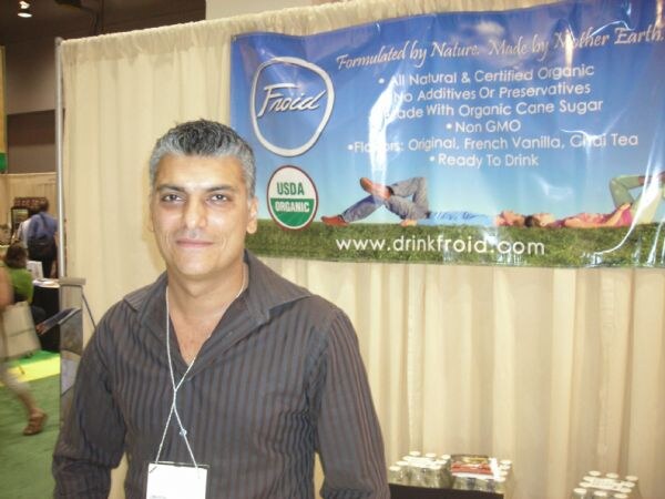 A gray-haired man in a dark striped shirt stands in front of a Froid banner reading Formulated by Nature, with a USDA Organic seal and the web address drinkfroid.com.