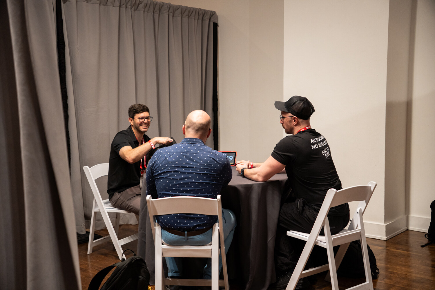 Three men at a round table, one in glasses laughing while the others talk.