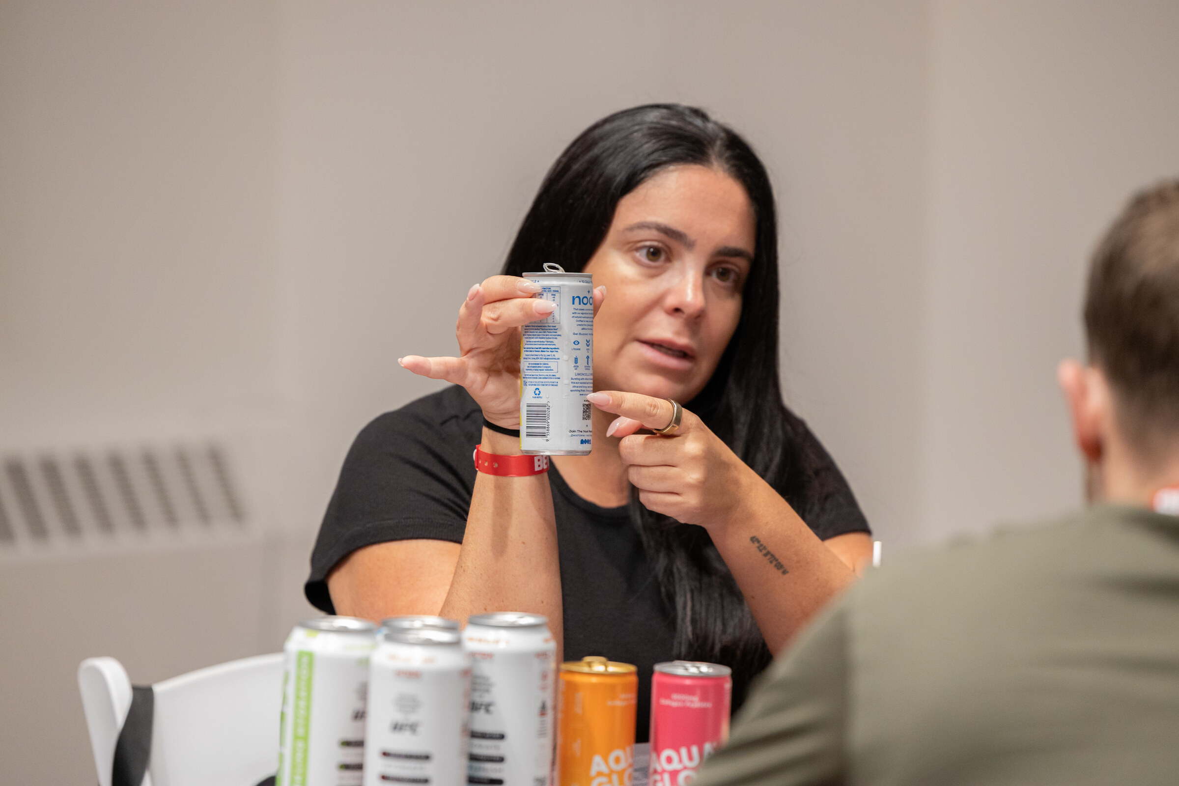Woman holding up a can and pointing to it while explaining, with a row of cans in the foreground.