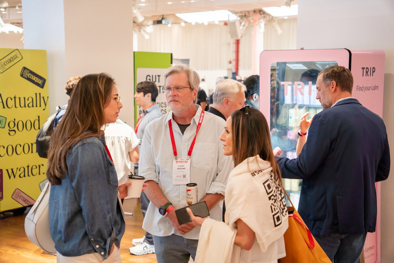 Four attendees talking near a yellow coaqua coconut water banner and a pink TRIP drinks fridge.