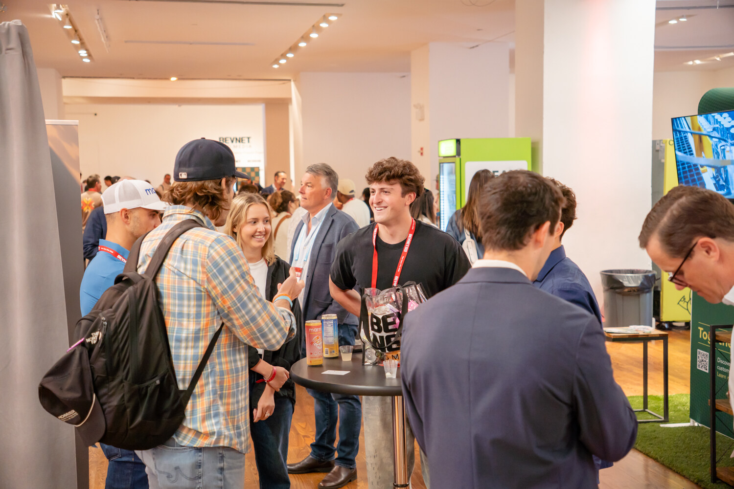 Group of young attendees around a high-top table of drinks, one in a backpack and plaid shirt.