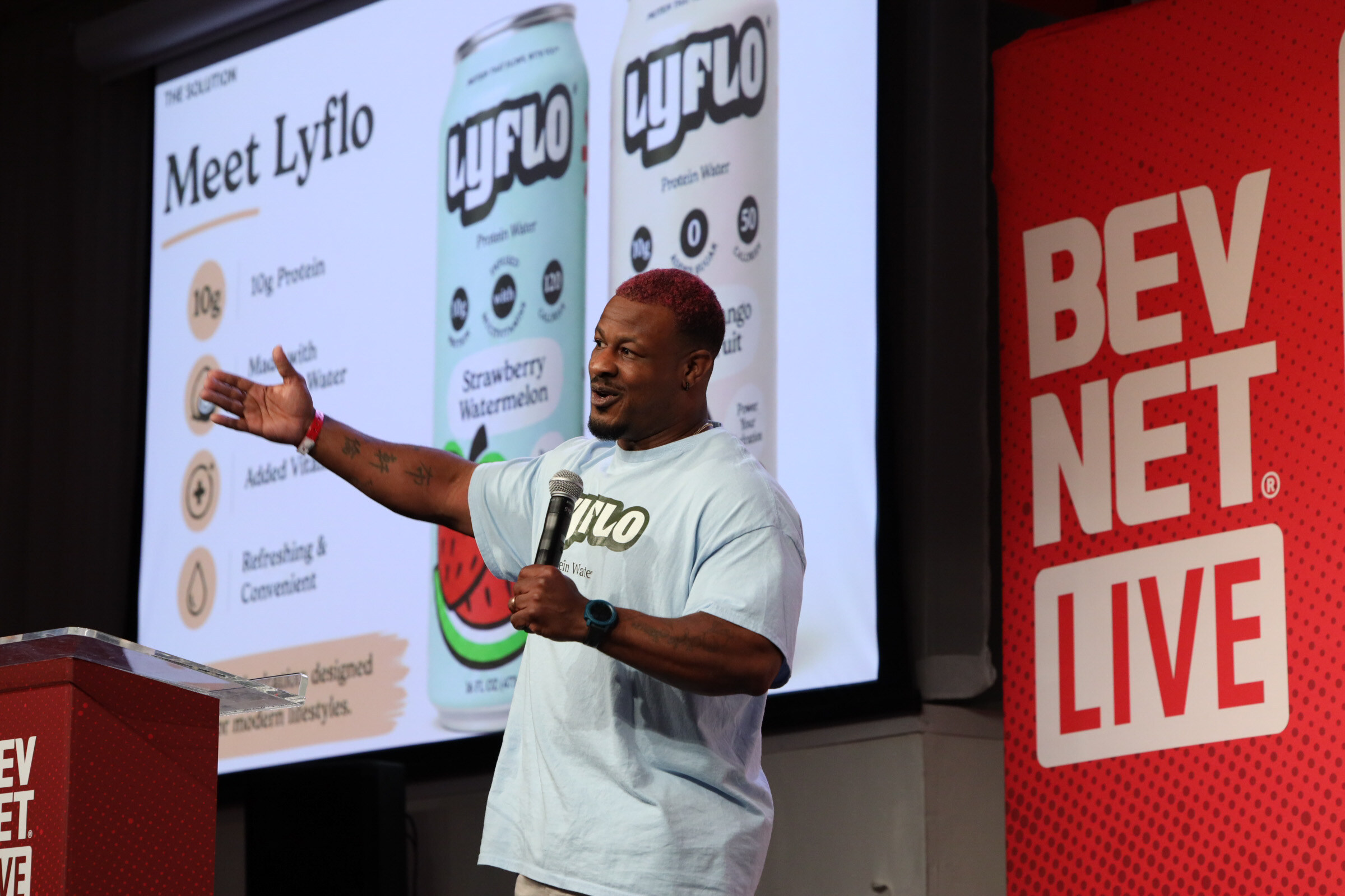 Man in a Lyflo T-shirt gestures toward a Meet Lyflo slide showing two cans of protein water.