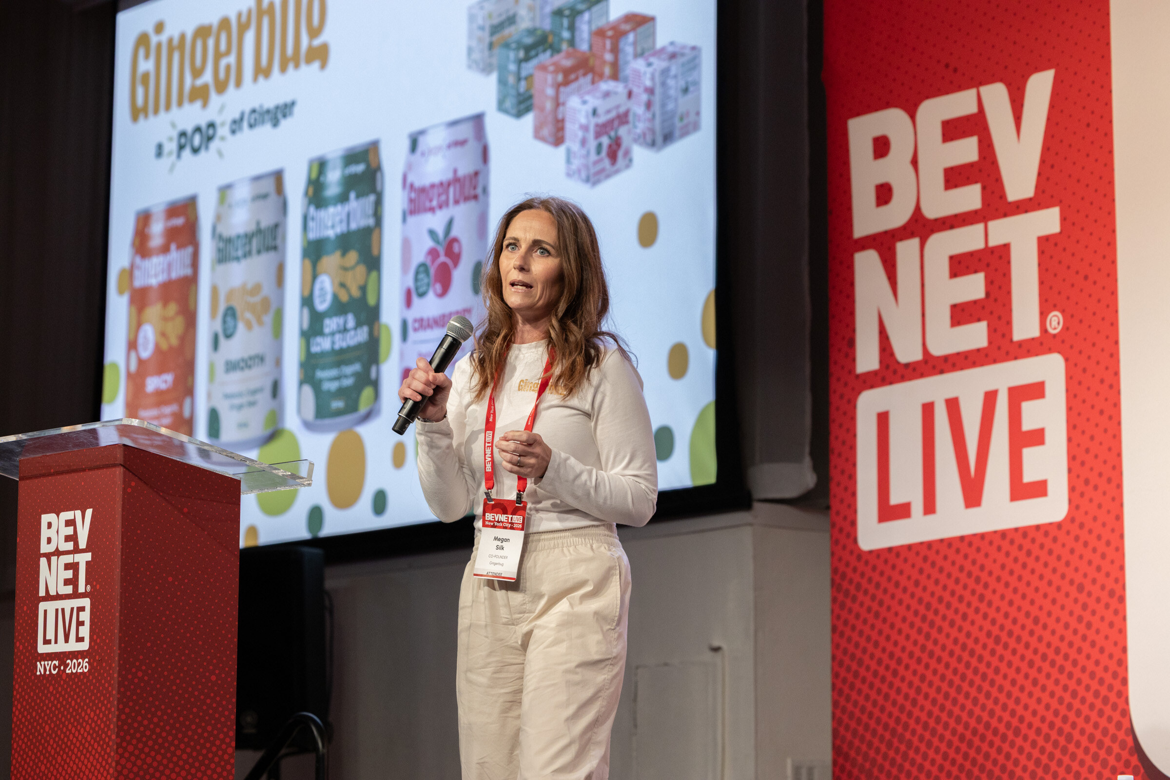 Woman in a cream sweater speaks into a microphone beside a slide of Gingerbug cans and a BevNET Live podium.