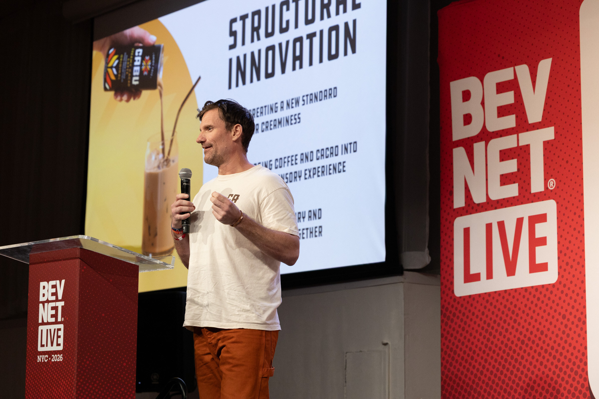 Man in a Cabu T-shirt speaks beside a podium in front of a Structural Innovation slide showing an iced coffee drink and a Cabu carton.