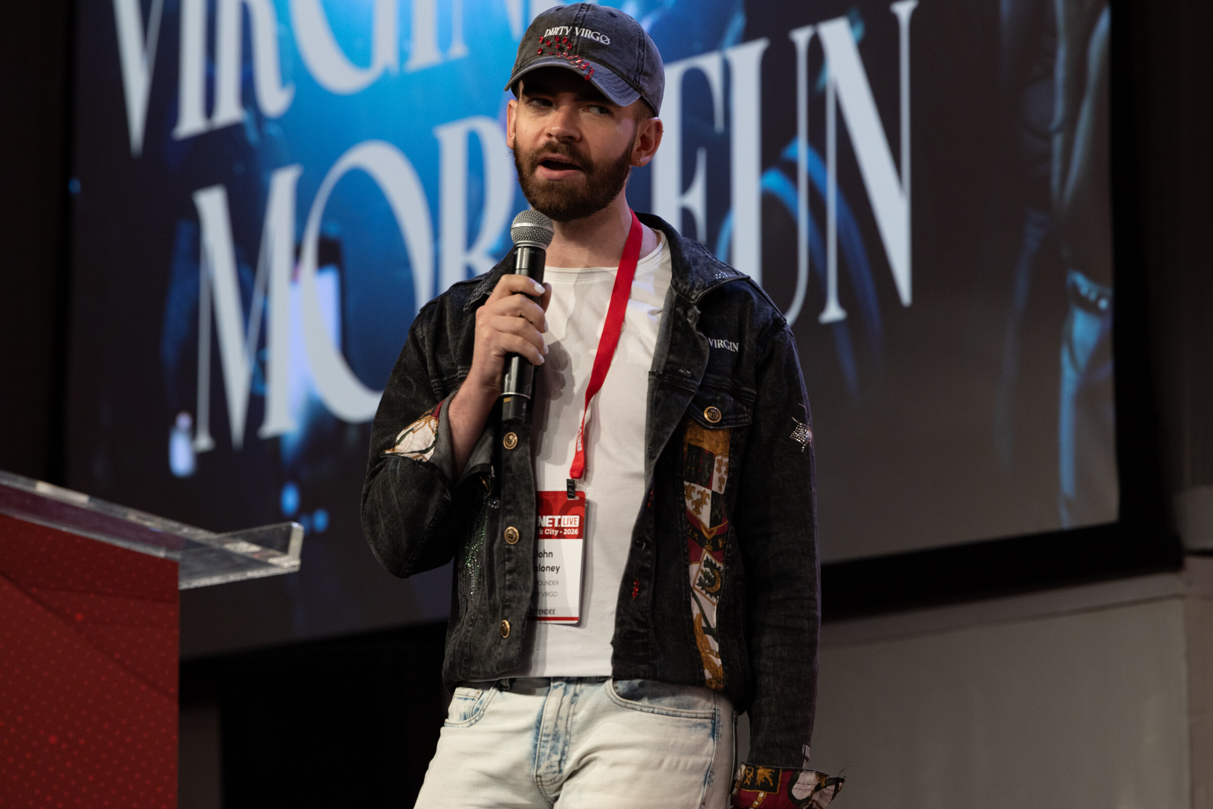 Man in a Dirty Virgo cap, denim jacket and BevNET Live lanyard speaks into a microphone.