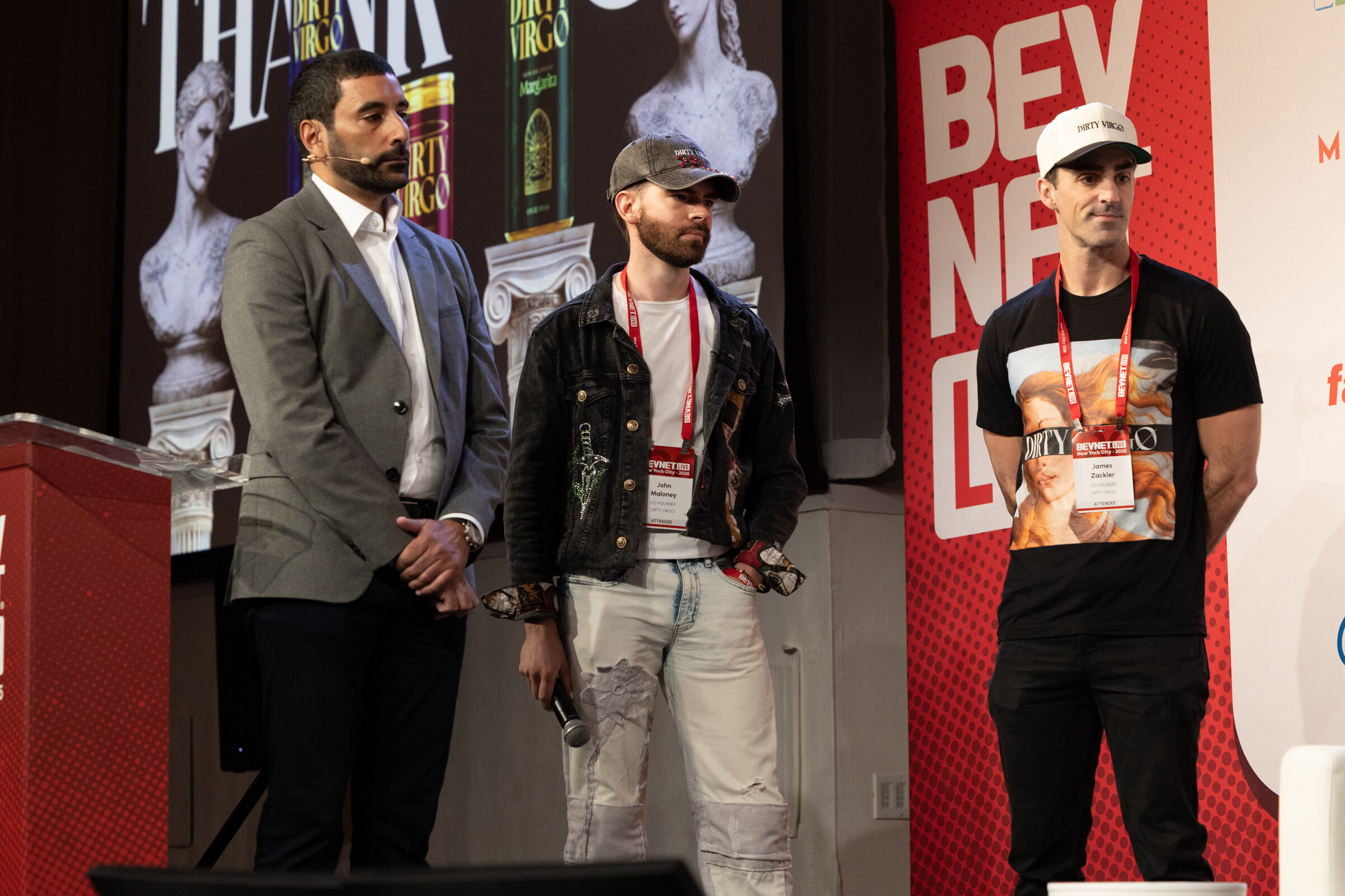 Host in a grey jacket stands with two men from Dirty Virgo on stage in front of a slide reading Thank You.