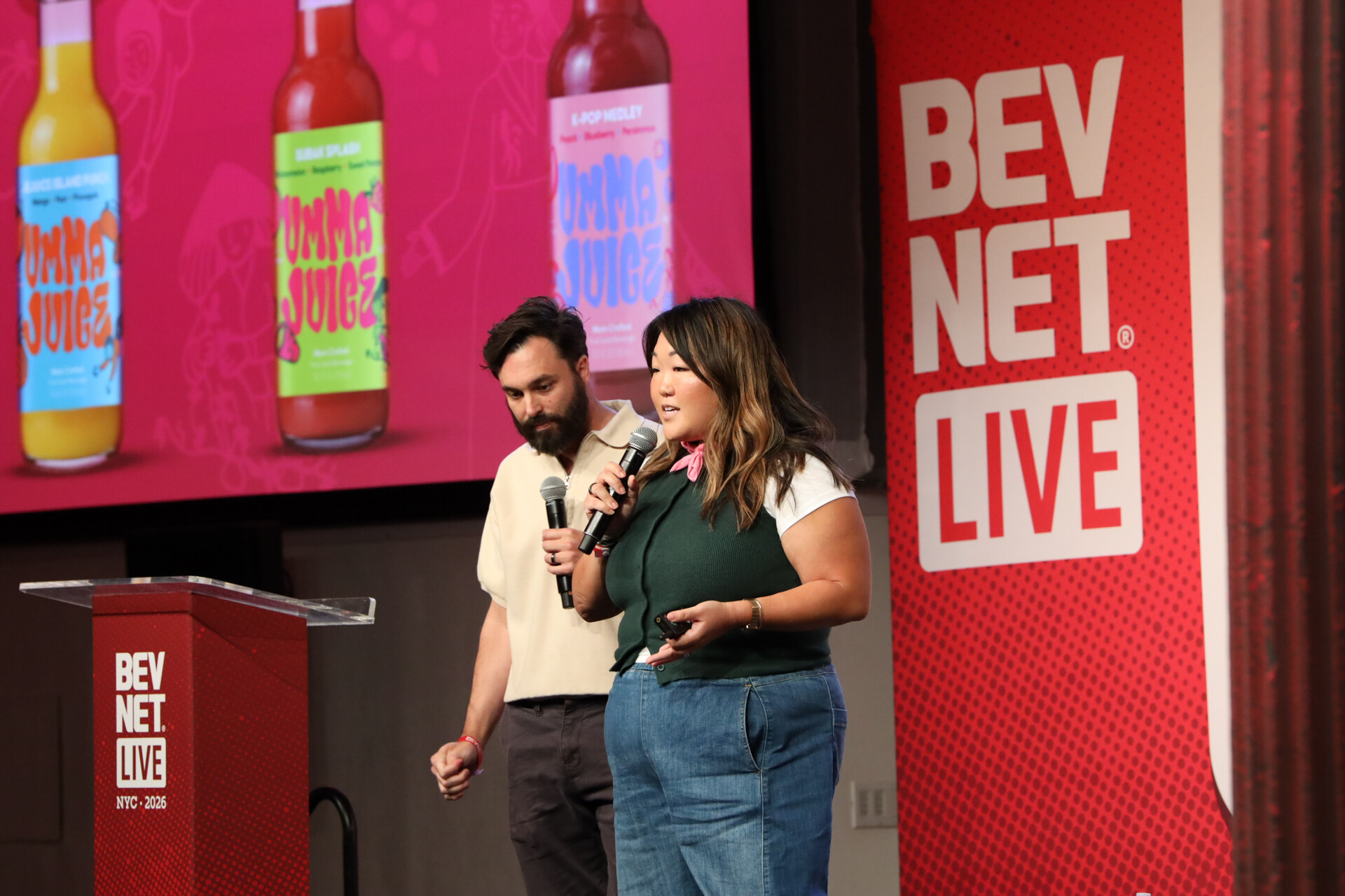 Man and woman with microphones present in front of a pink slide with three bottles of Umma Juice.
