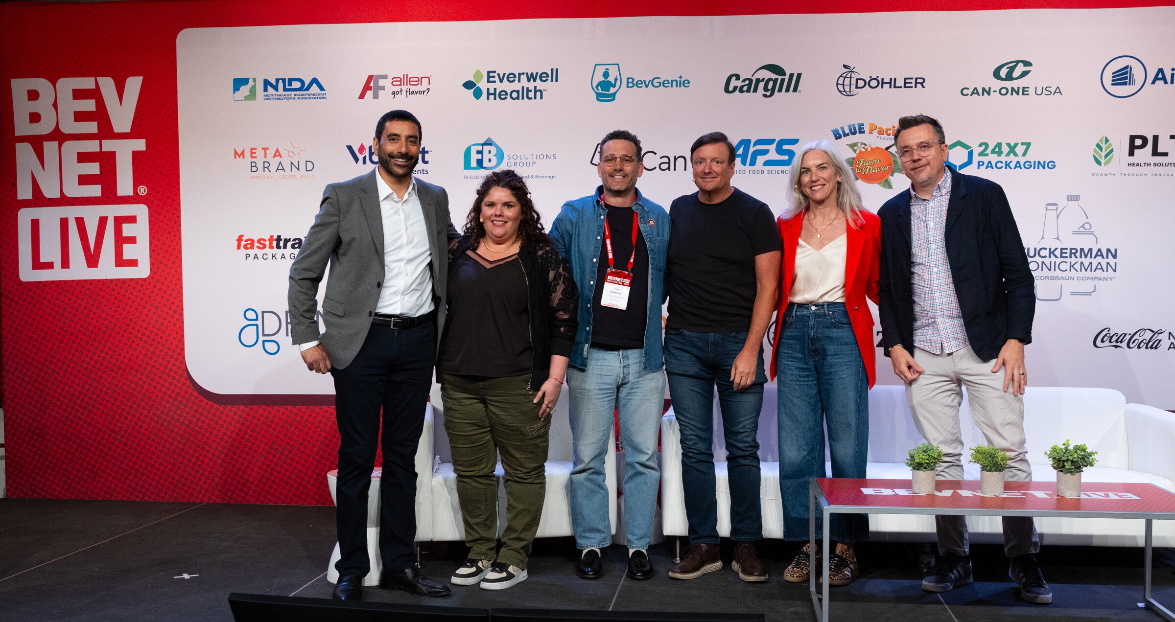 Six people smile in a line on stage in front of the BevNET Live sponsor wall.