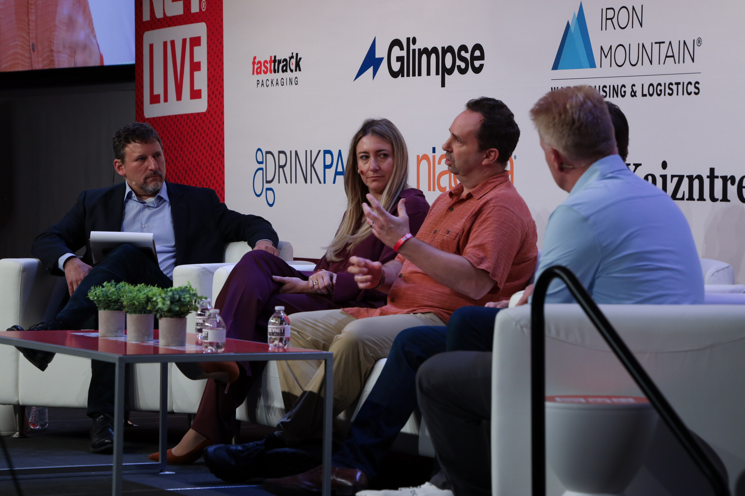 Four panelists on white couches, one gesturing as he speaks, in front of sponsor logos including Glimpse, Iron Mountain and DrinkPAK.