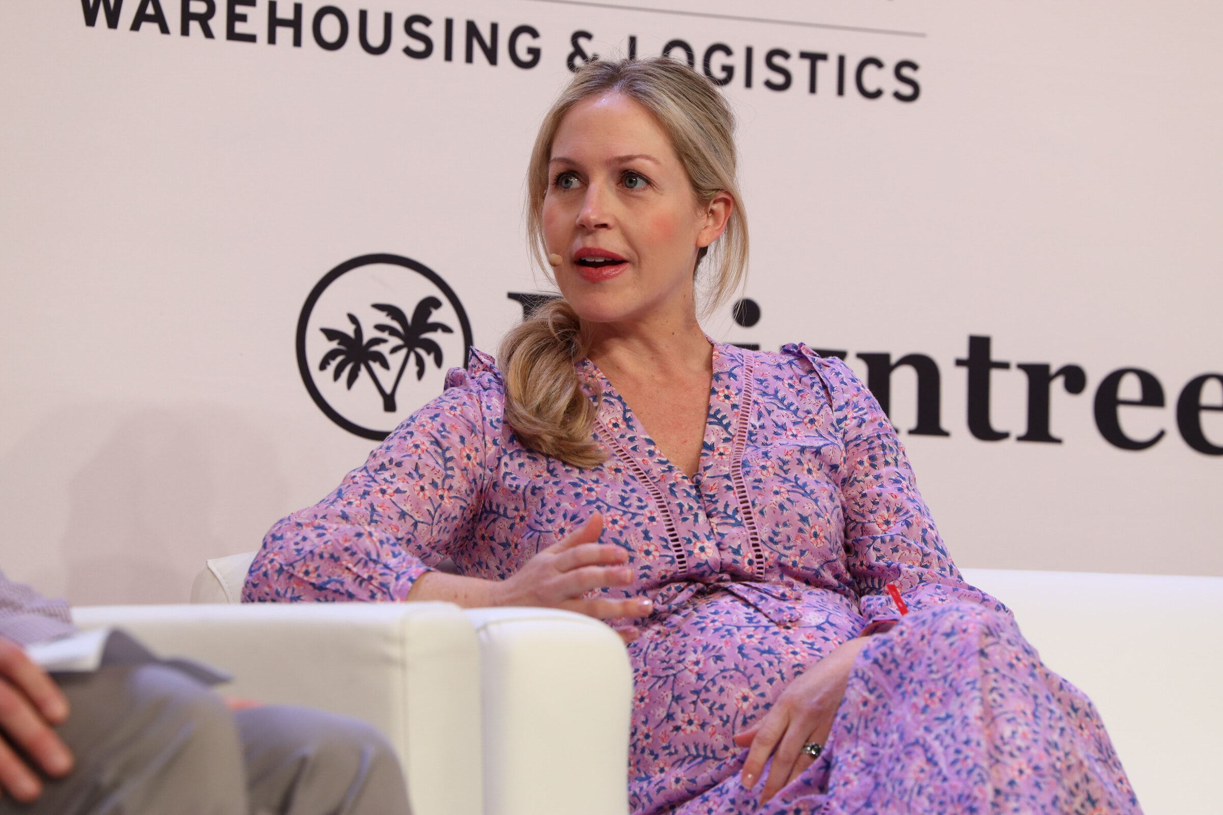 Woman in a purple floral dress speaking from a white couch in front of a Kaizntree logo.