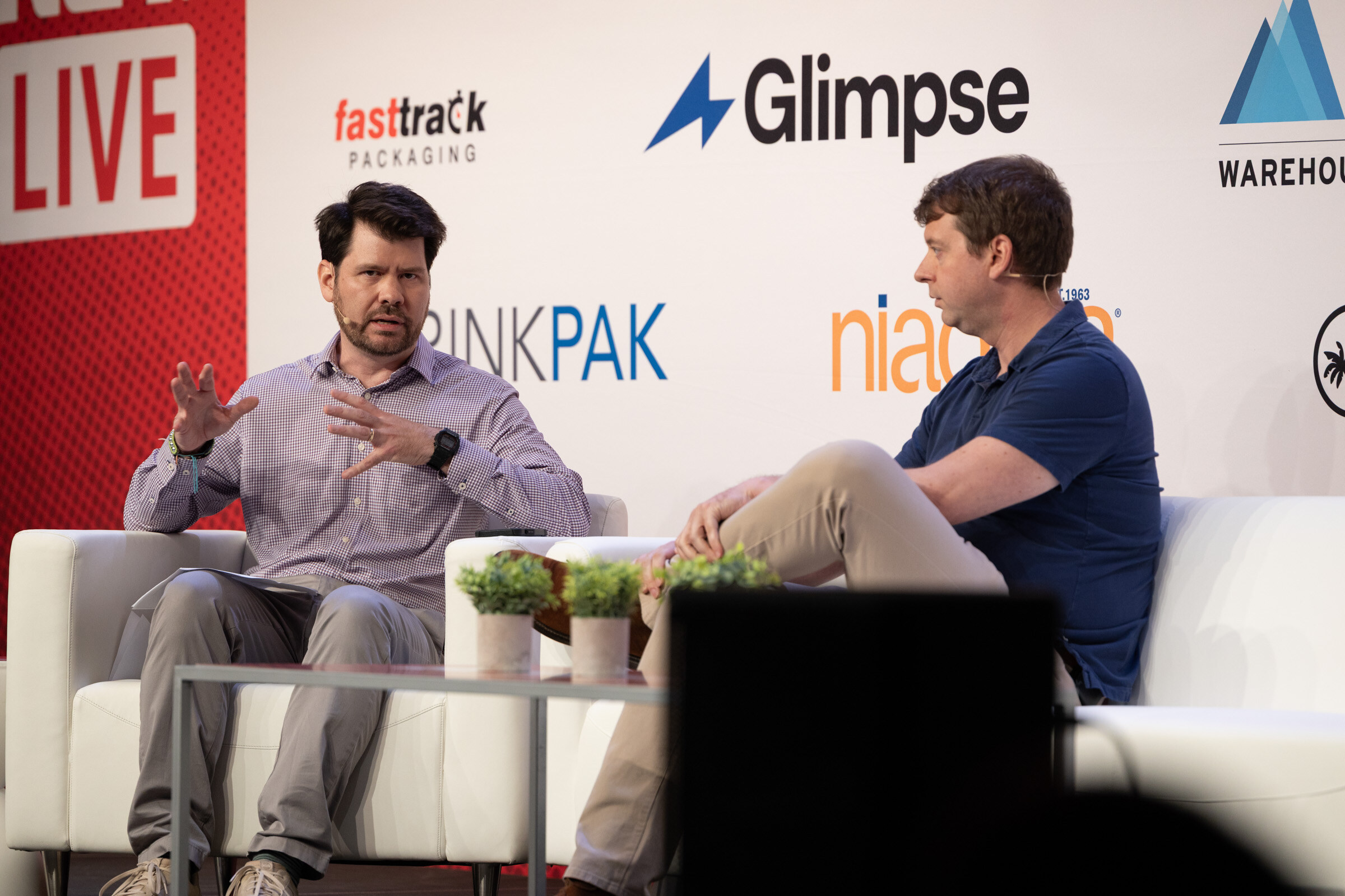 Two men seated on white couches in conversation, one gesturing, in front of Glimpse and DrinkPAK logos.