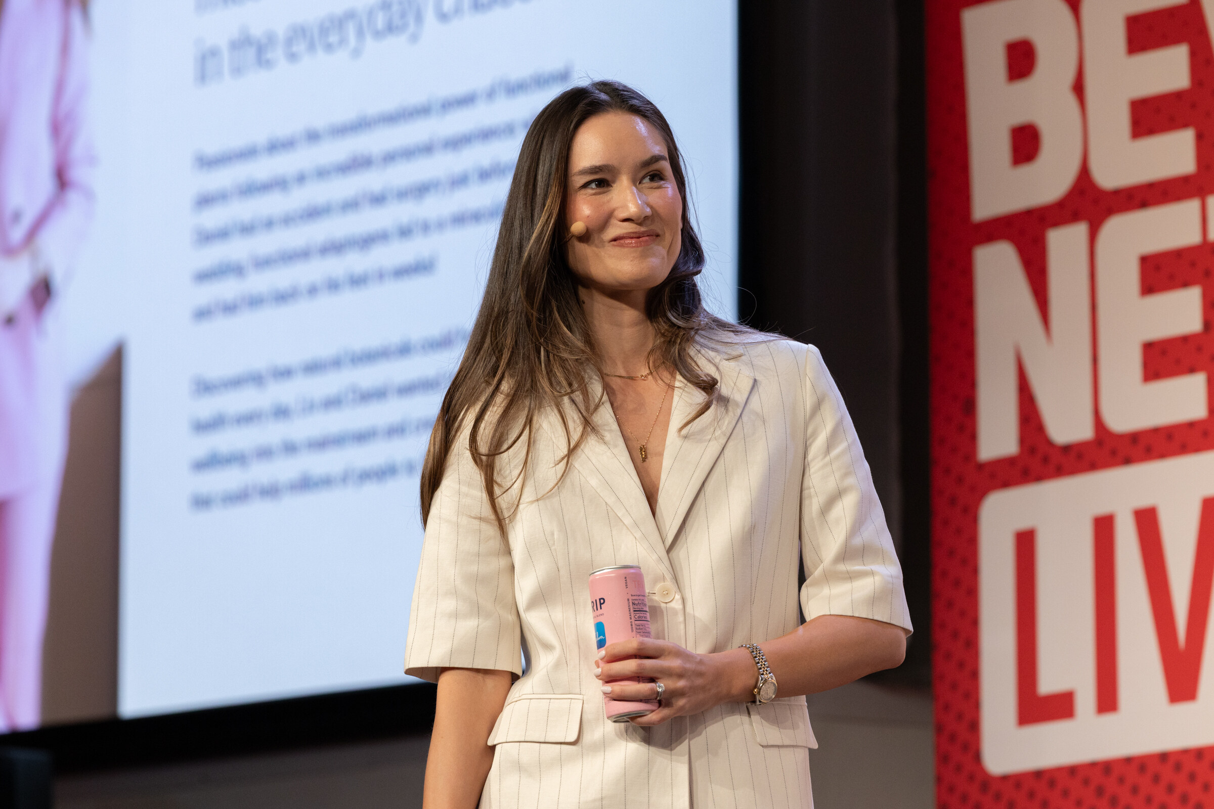 Smiling woman in a cream pinstripe suit holding a pink TRIP can in front of a large screen and a BevNET Live banner.