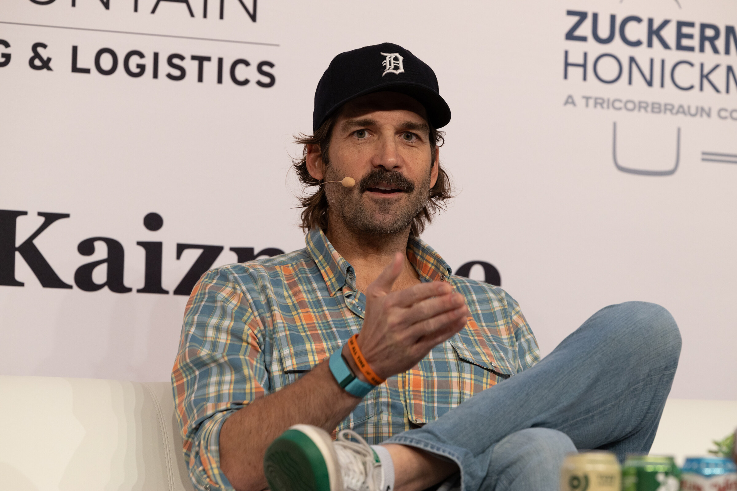Man with a mustache in a black baseball cap and plaid shirt gesturing as he speaks.