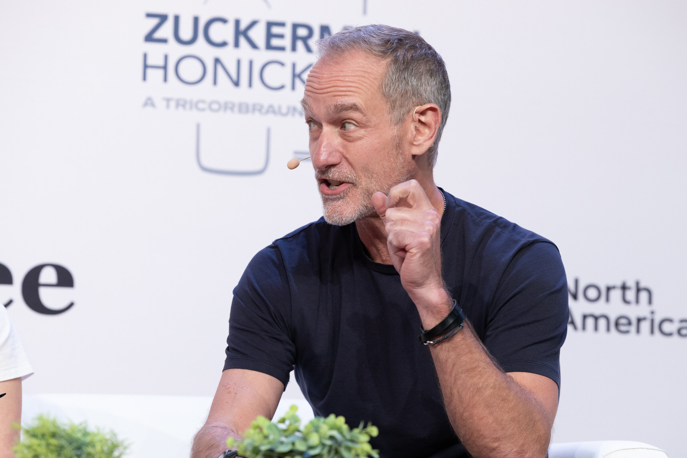 Man with gray hair in a navy T-shirt speaking with his hand raised to his chin.