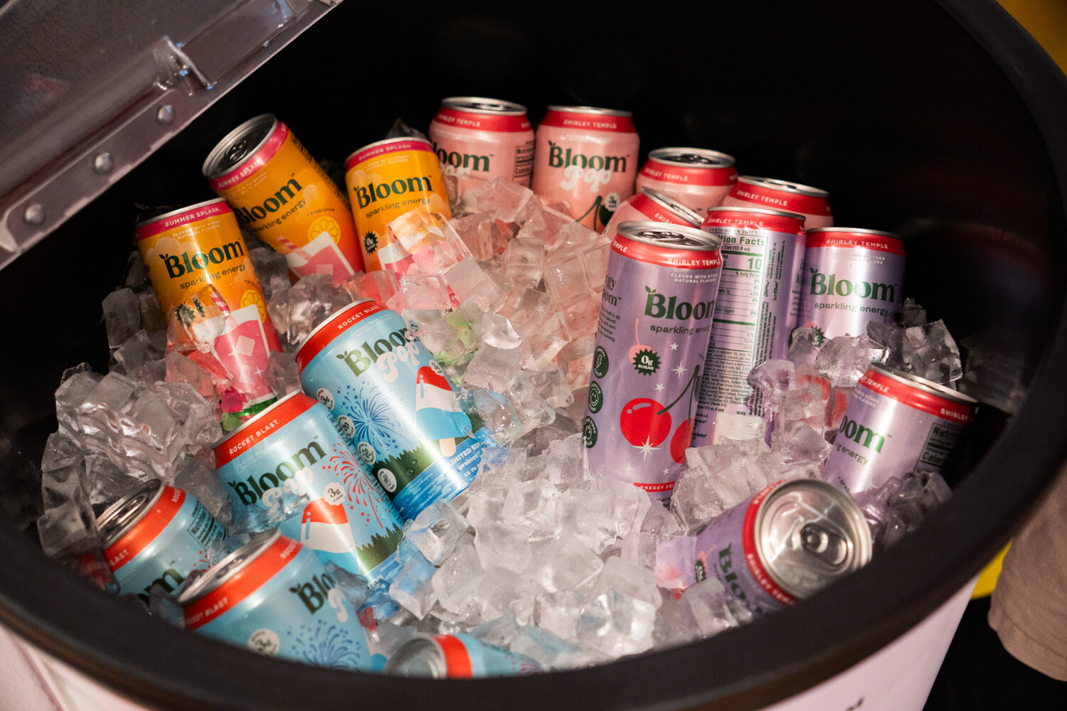Colorful Bloom cans packed in ice inside a round cooler.