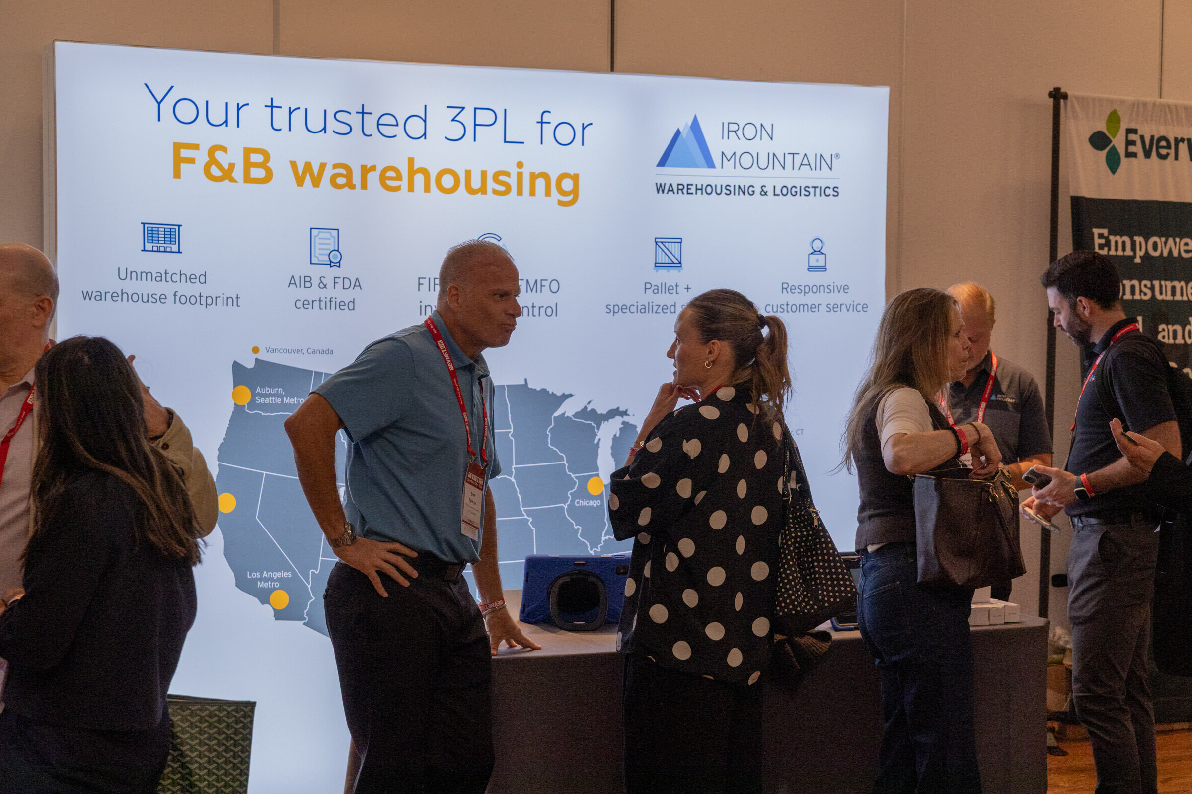 Several attendees talk in front of a light blue Iron Mountain backdrop reading "Your trusted 3PL for F&B warehousing."
