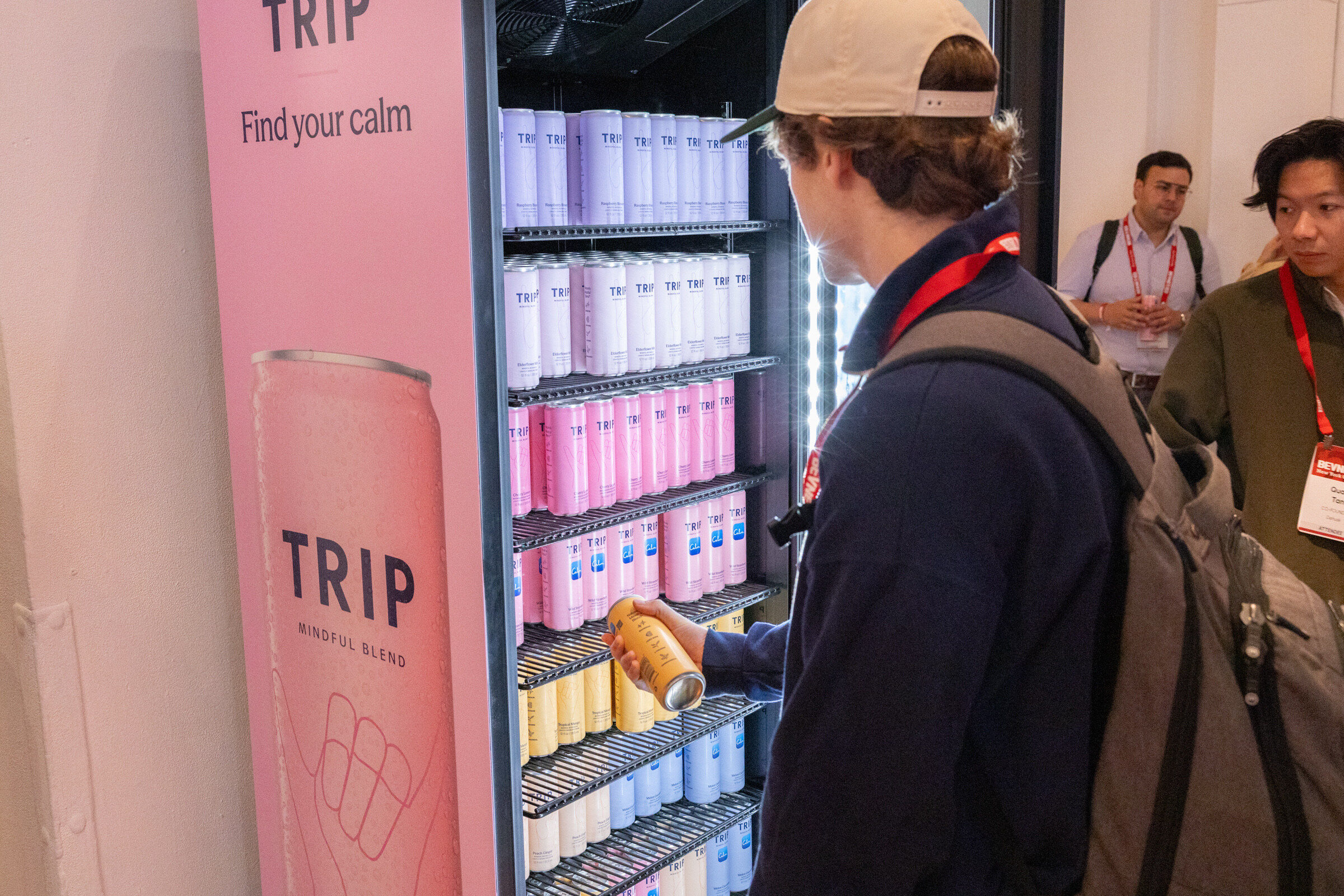 Man in a cap reaches for a can in a pink TRIP fridge stocked with pastel cans.