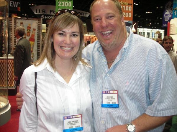 Micah Bingeman of Talking Rain Beverage, left, and Bruce Trent of Talking Rain Beverage, right, smile together in an aisle of the show floor, both wearing show badges.