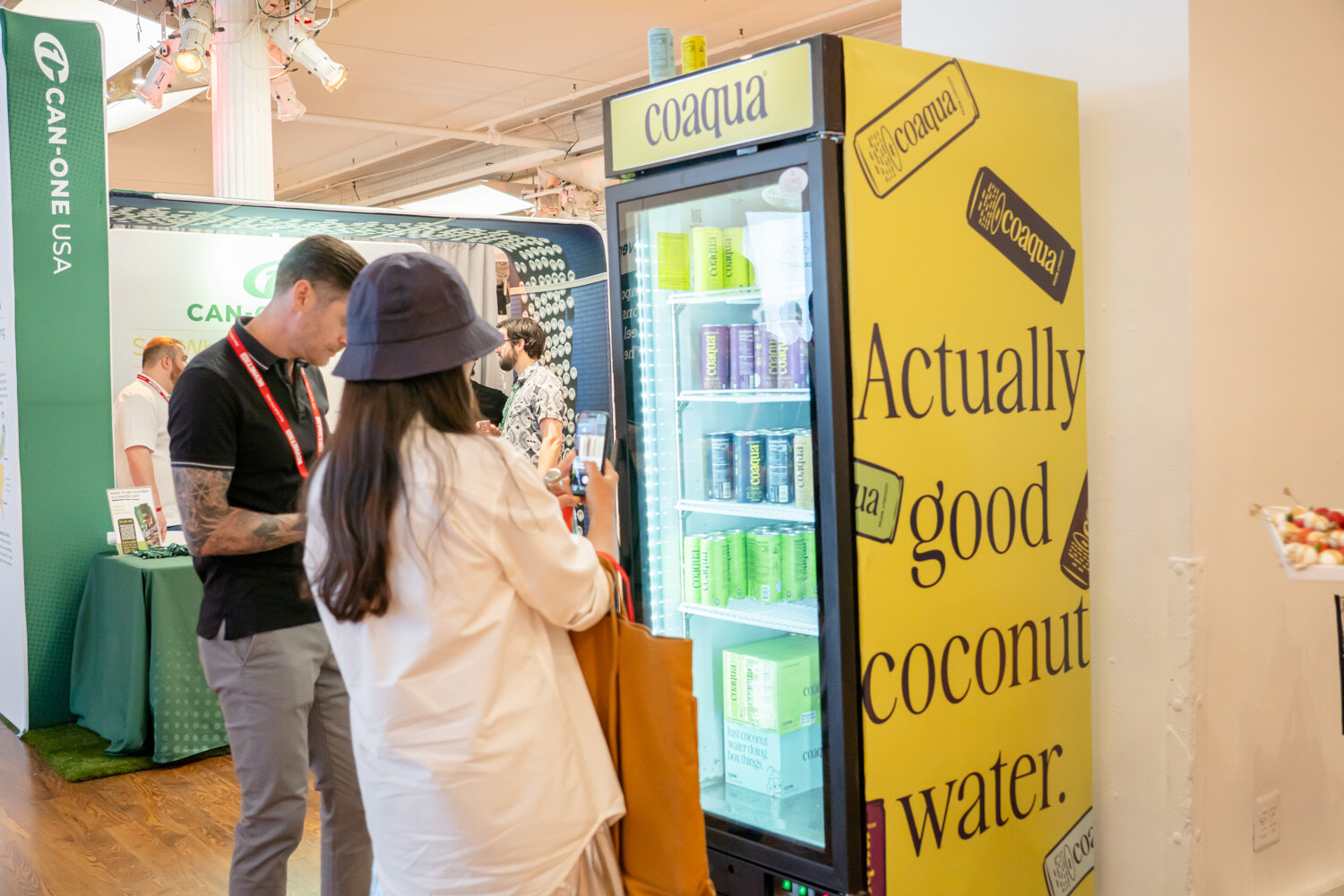 Two attendees browse a yellow coaqua fridge reading "Actually good coconut water."