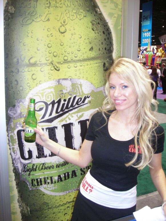 A smiling woman with long blonde hair in a black top holds a green bottle of Miller Chill beside a large Miller Chill bottle graphic labeled Chelada Style.