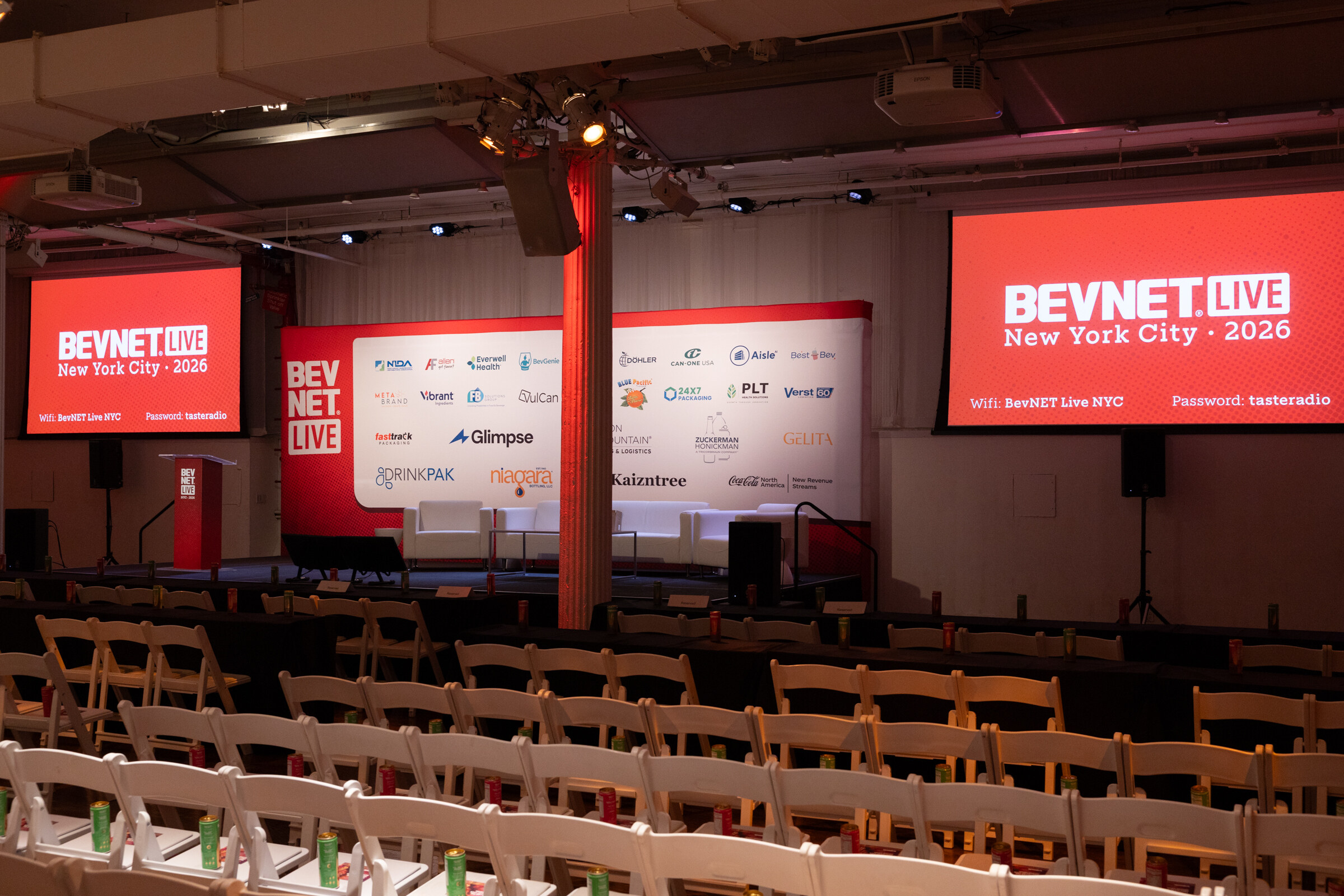 Stage framed by screens reading BevNET Live New York City 2026 above rows of empty white chairs.