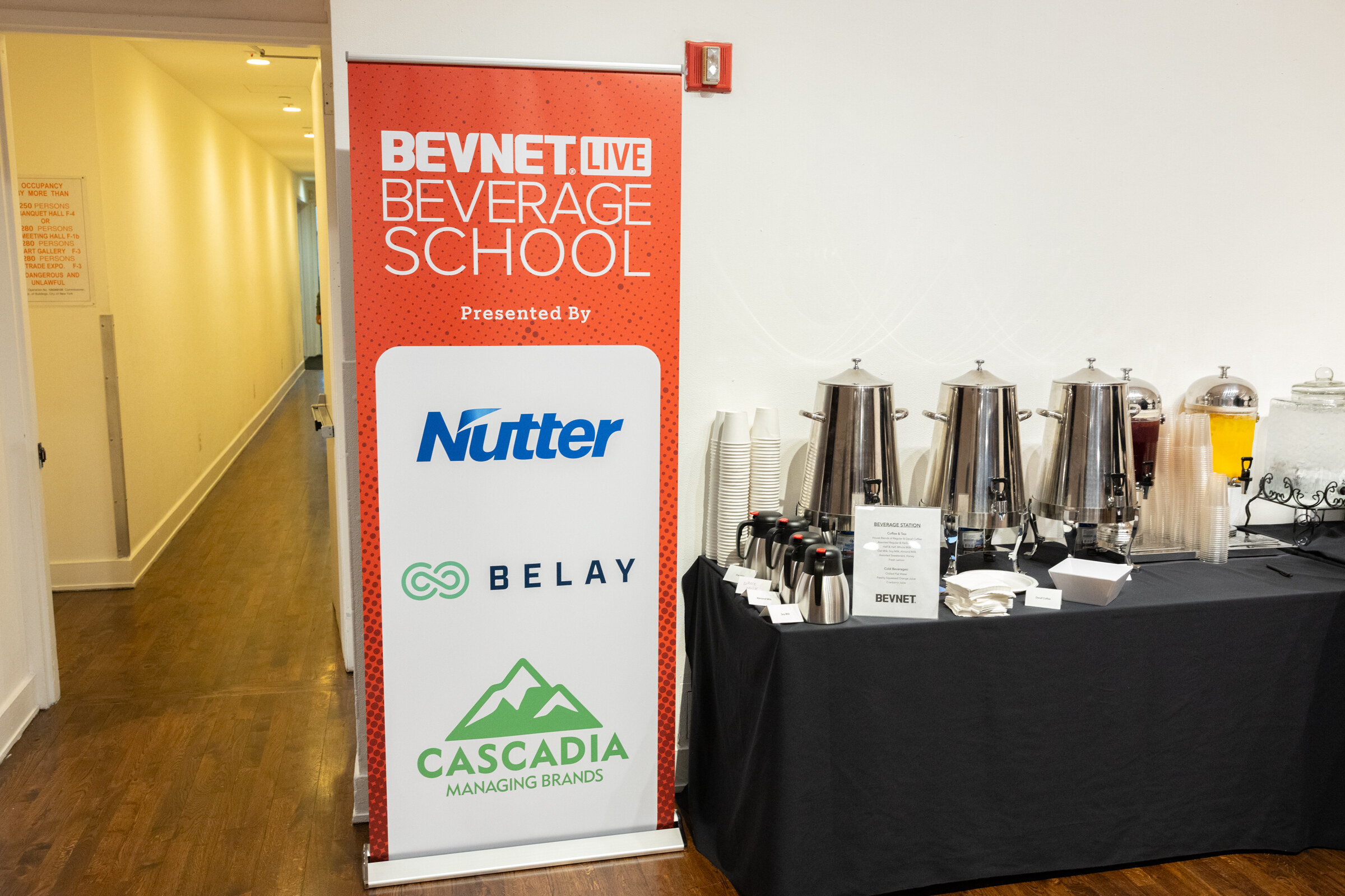 BevNET Live Beverage School banner beside a coffee and juice station on a black table.