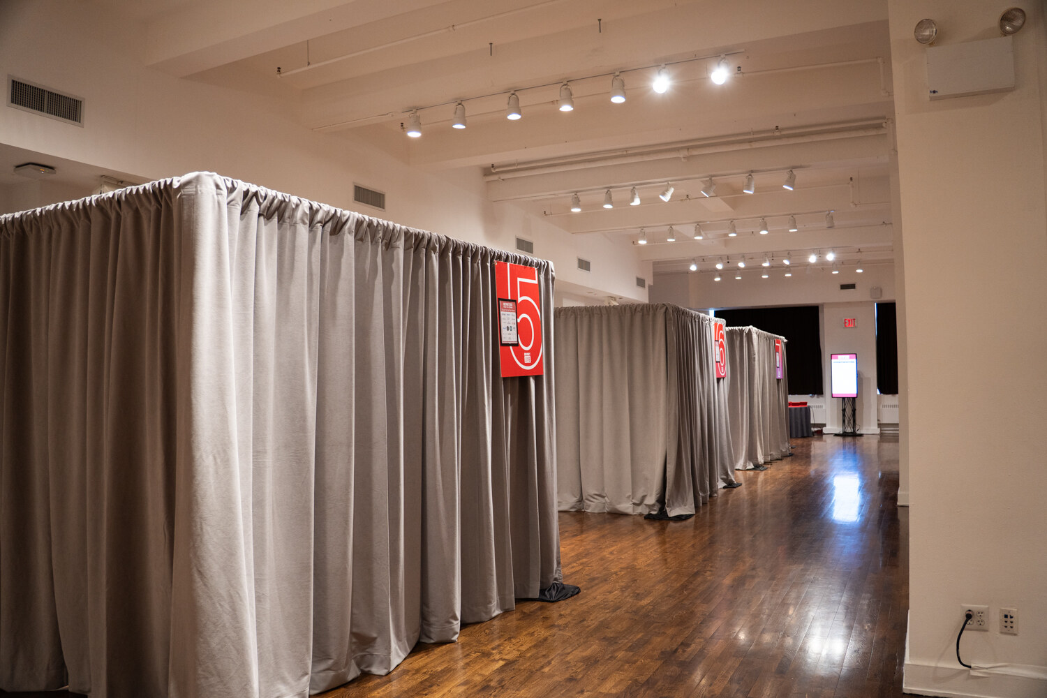 Row of gray curtained booths marked with red number signs on a hardwood floor.