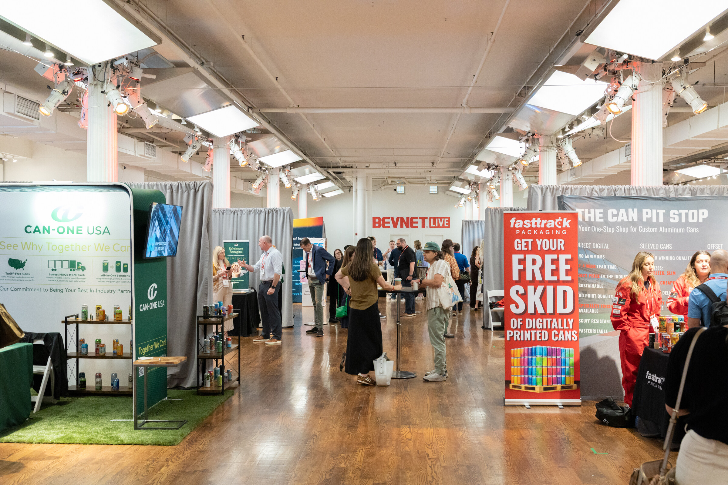 Wide view of a busy expo floor with a green Can-One USA booth and a fasttrack Packaging banner.