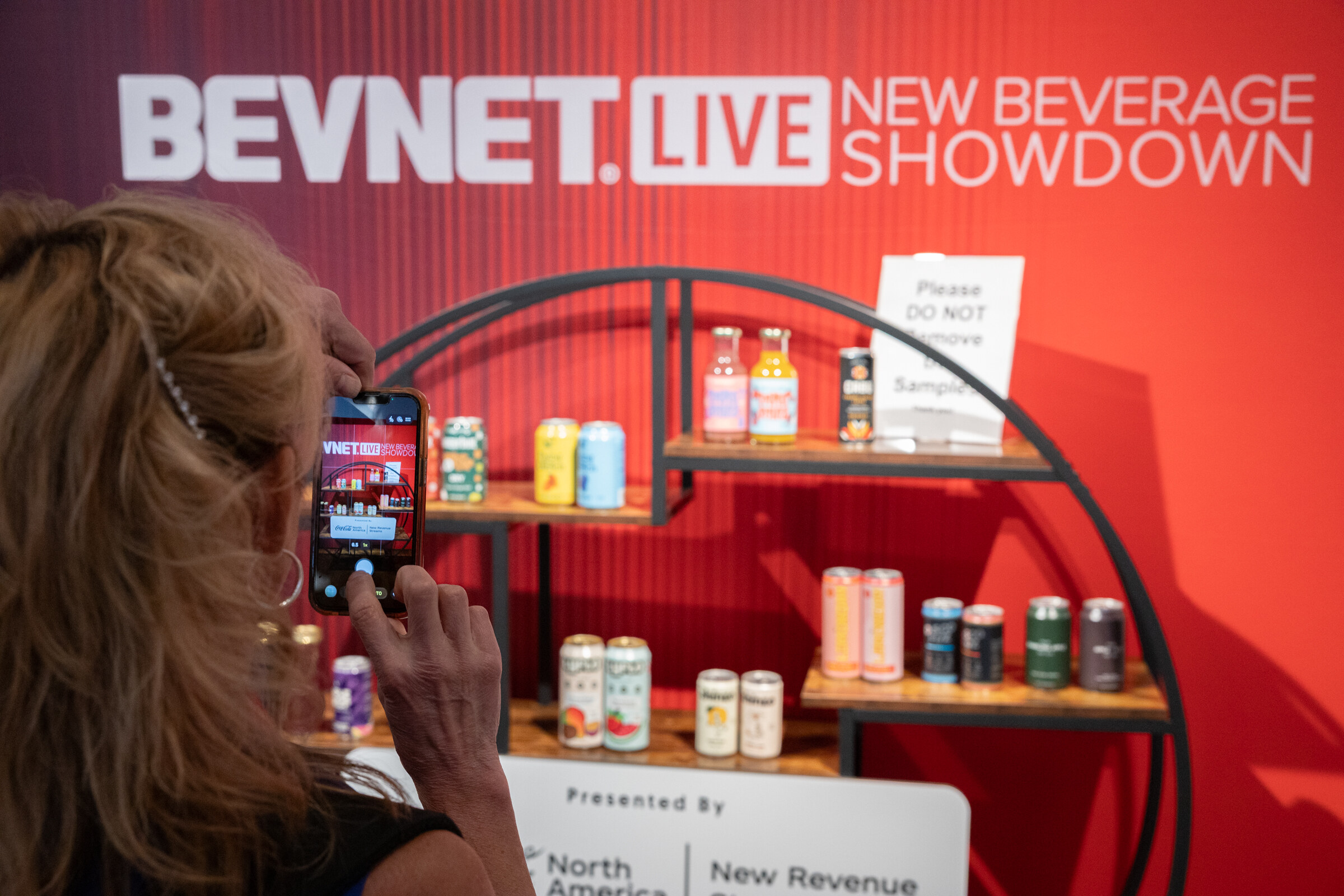 Woman photographing the New Beverage Showdown shelf of products with her phone.