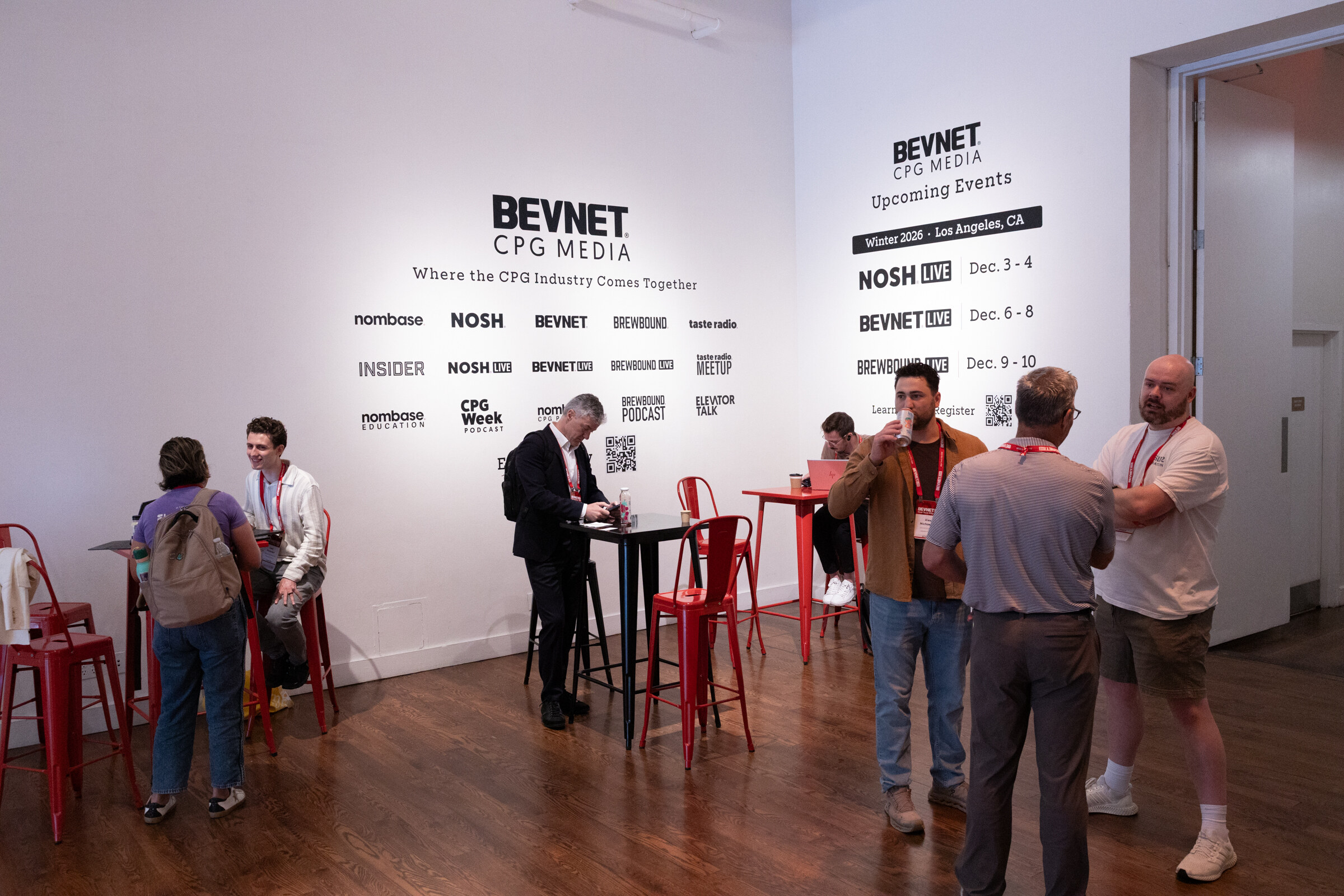 Attendees talking at red and black high-top tables in front of a white wall listing BevNET CPG Media brands and upcoming events.