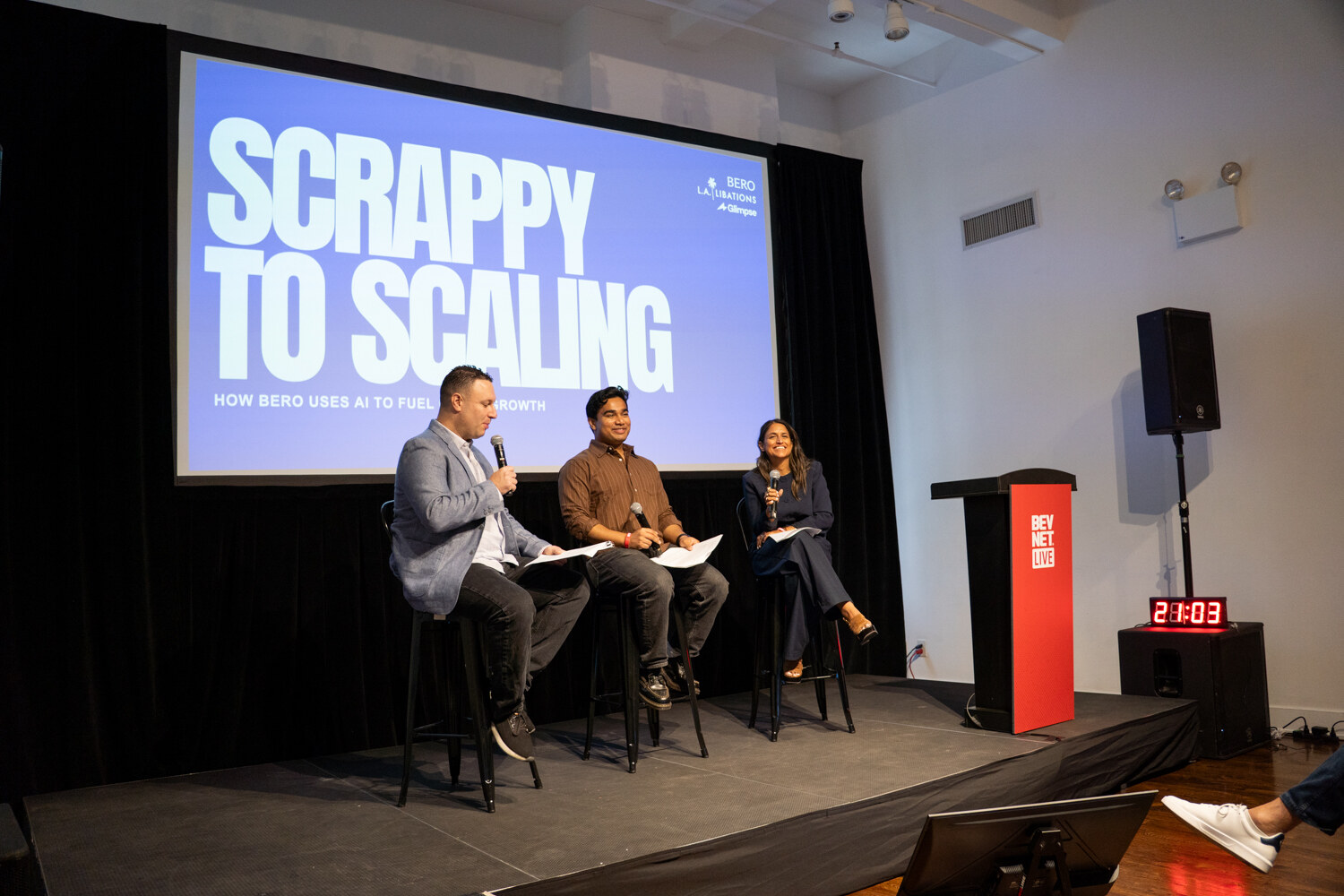 Three panelists on stools with microphones in front of a “Scrappy to Scaling” slide, next to a red BevNET Live podium.