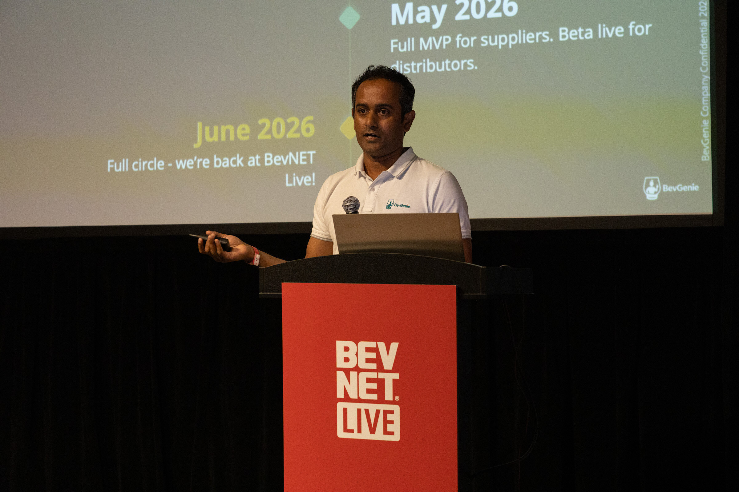 Man in a white BevGenie polo at a red BevNET Live podium beside a timeline slide.
